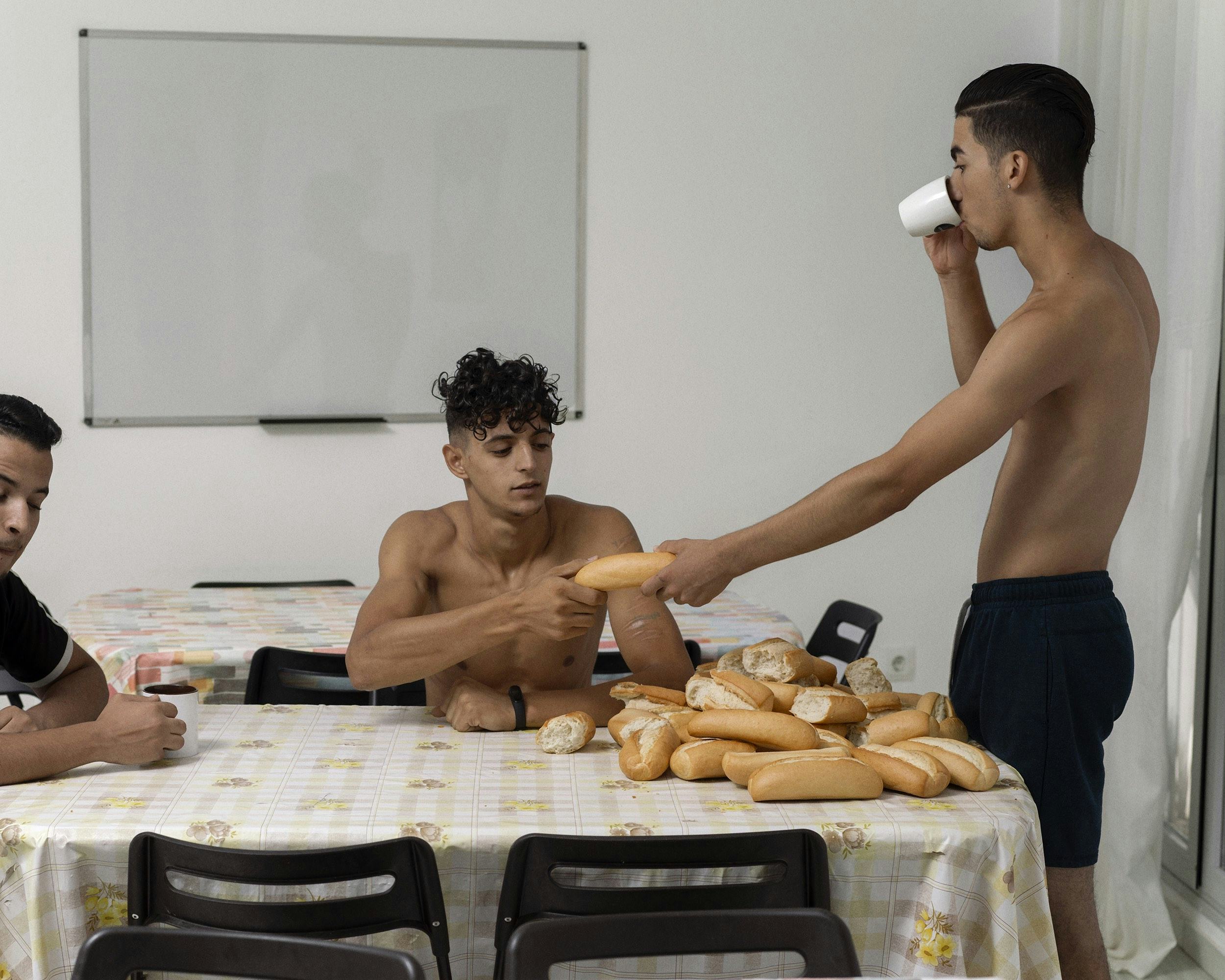 Image of three men, sitting and standing around a table full of small loafs of bread. © Felipe Romero Beltrán