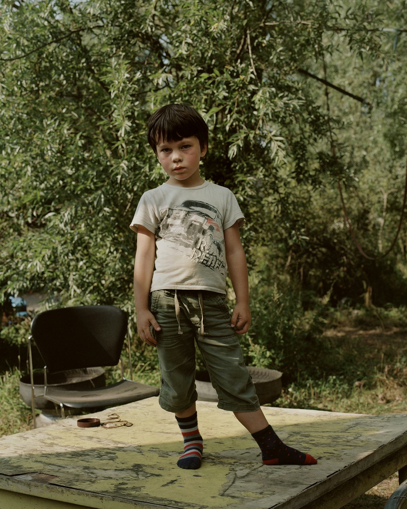 Little boy with brown hair and two different socks standing on a table in nature