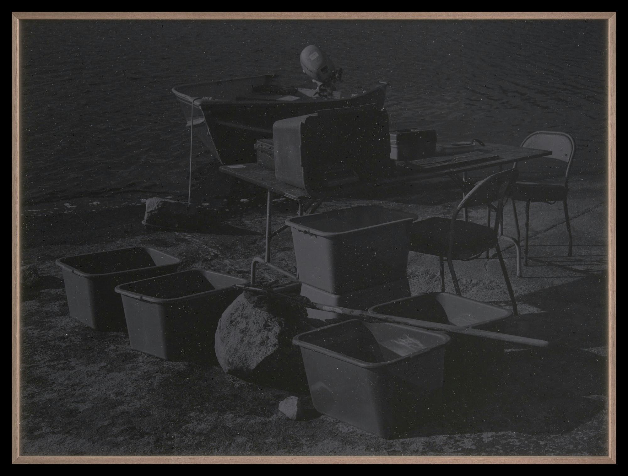 Dark picture of a table next to the lake. The table is surrounded by few objects such as chairs, pots and shovel