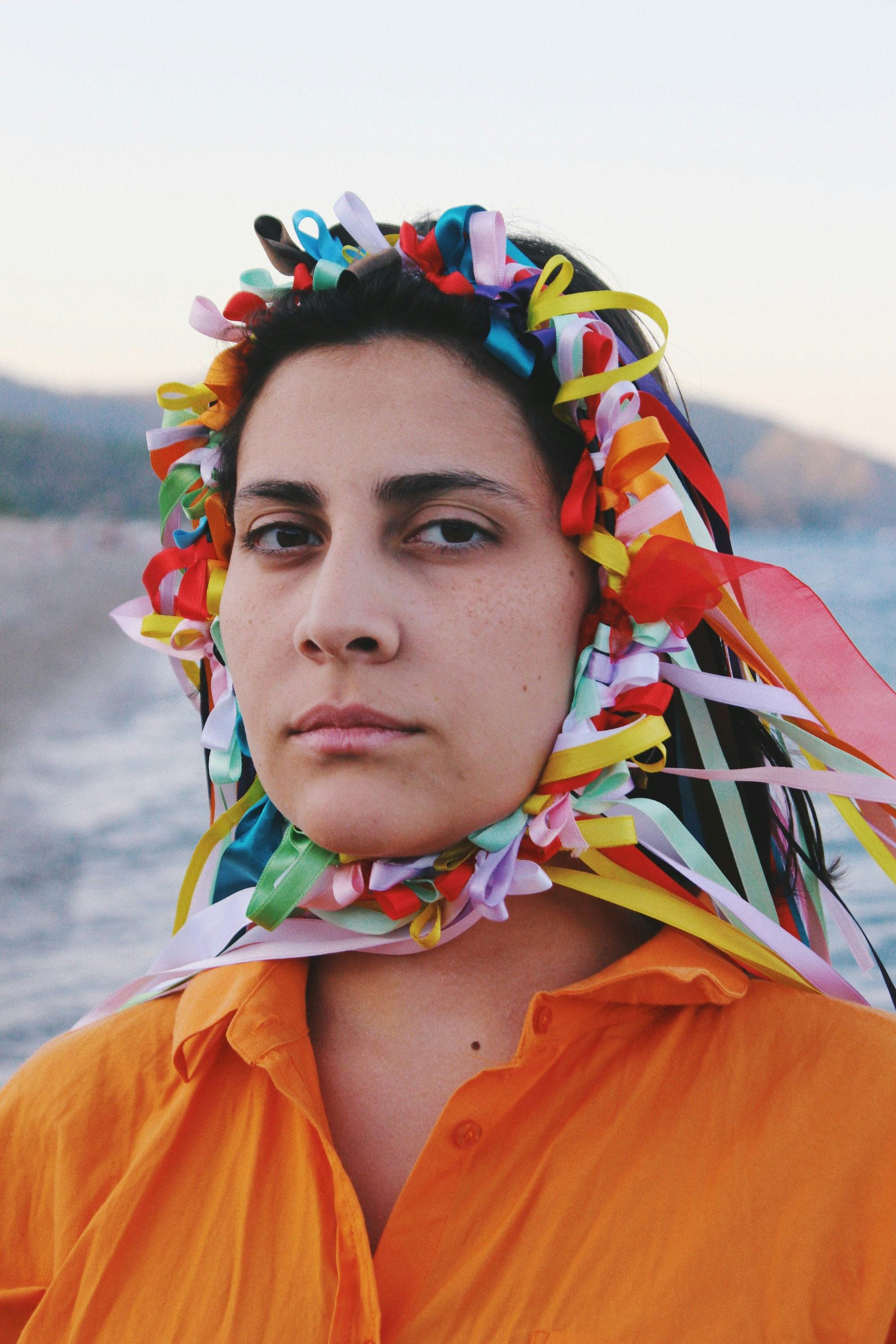 Portrait of a woman wearing an orange shirt, and a crown made of colourful ribbons. © Alp Peker
