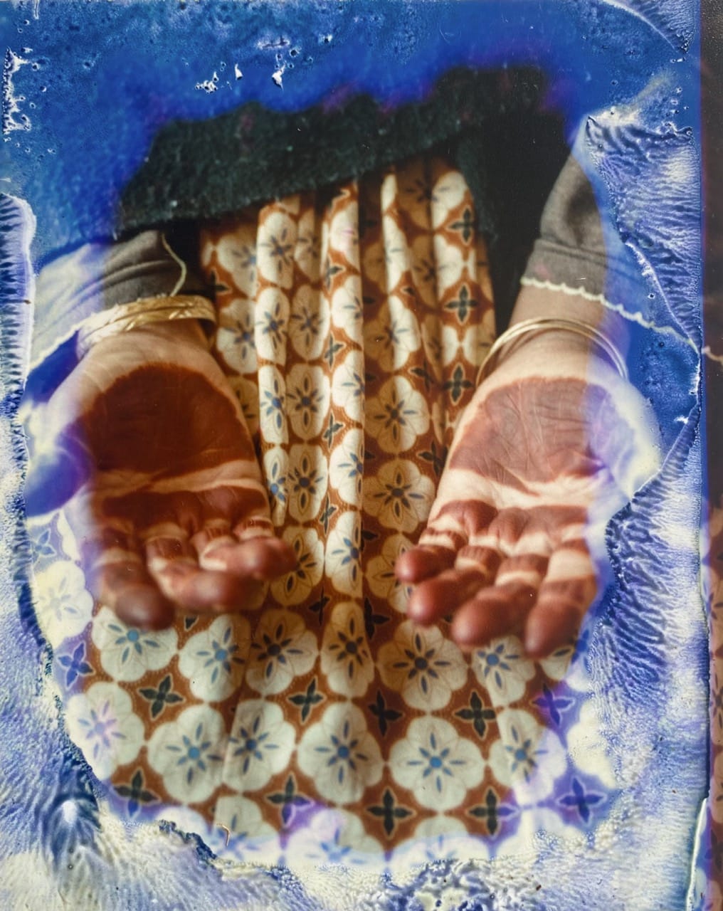 Hands cupped together over a patterned fabric, surrounded by a blue and white artistic border effect.