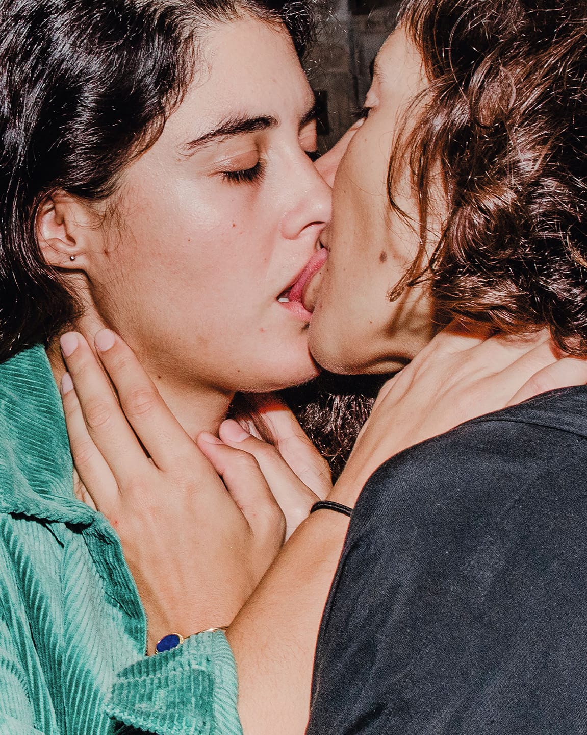 Two people kissing closely, with one wearing a green jacket. Their hands gently touch each other's necks, conveying intimacy.
