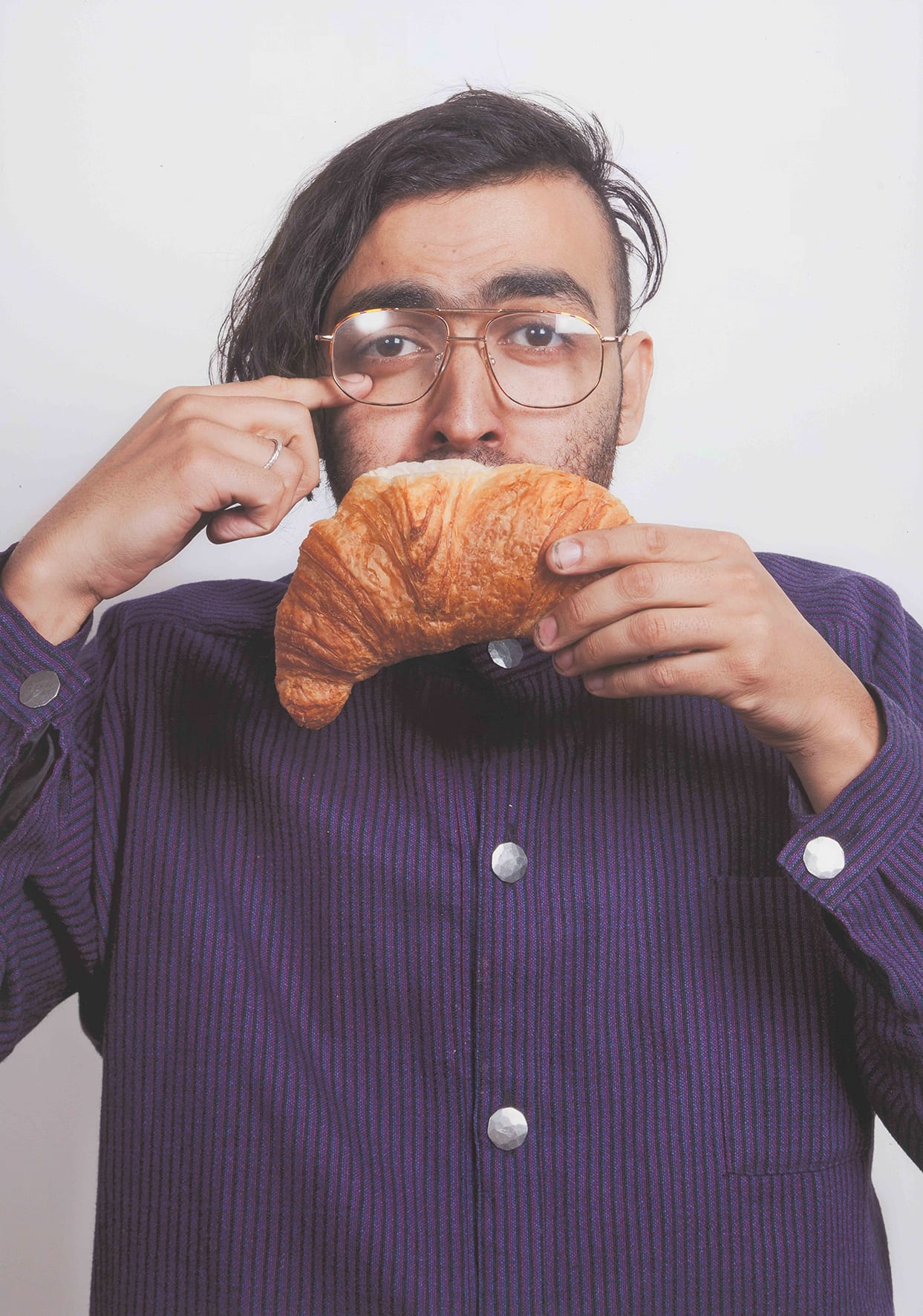 Man in een paars gestreepte blouse met croissant voor zijn mond.