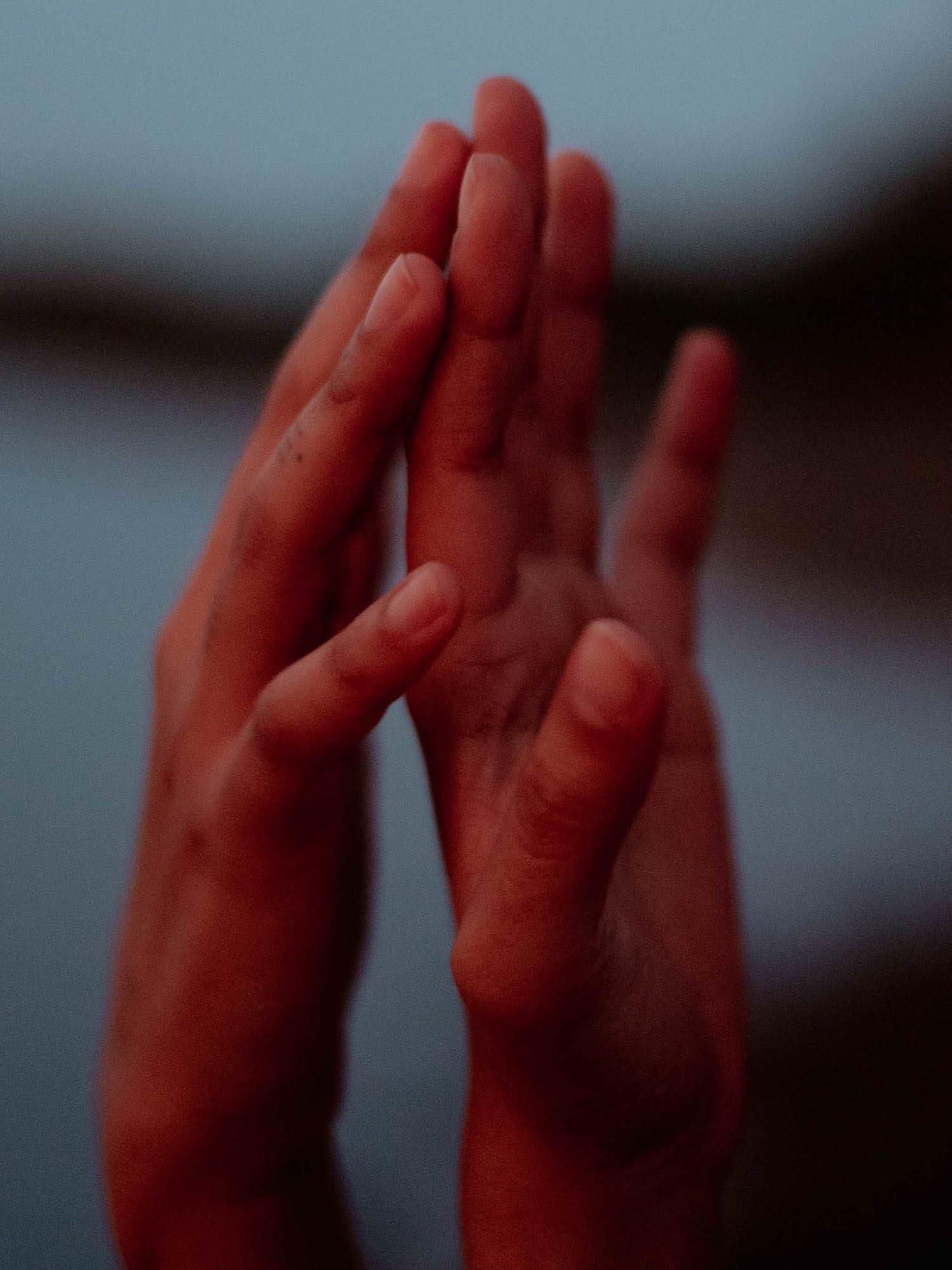 Two hands with fingers gently touching, set against a dimly lit, blurred background.