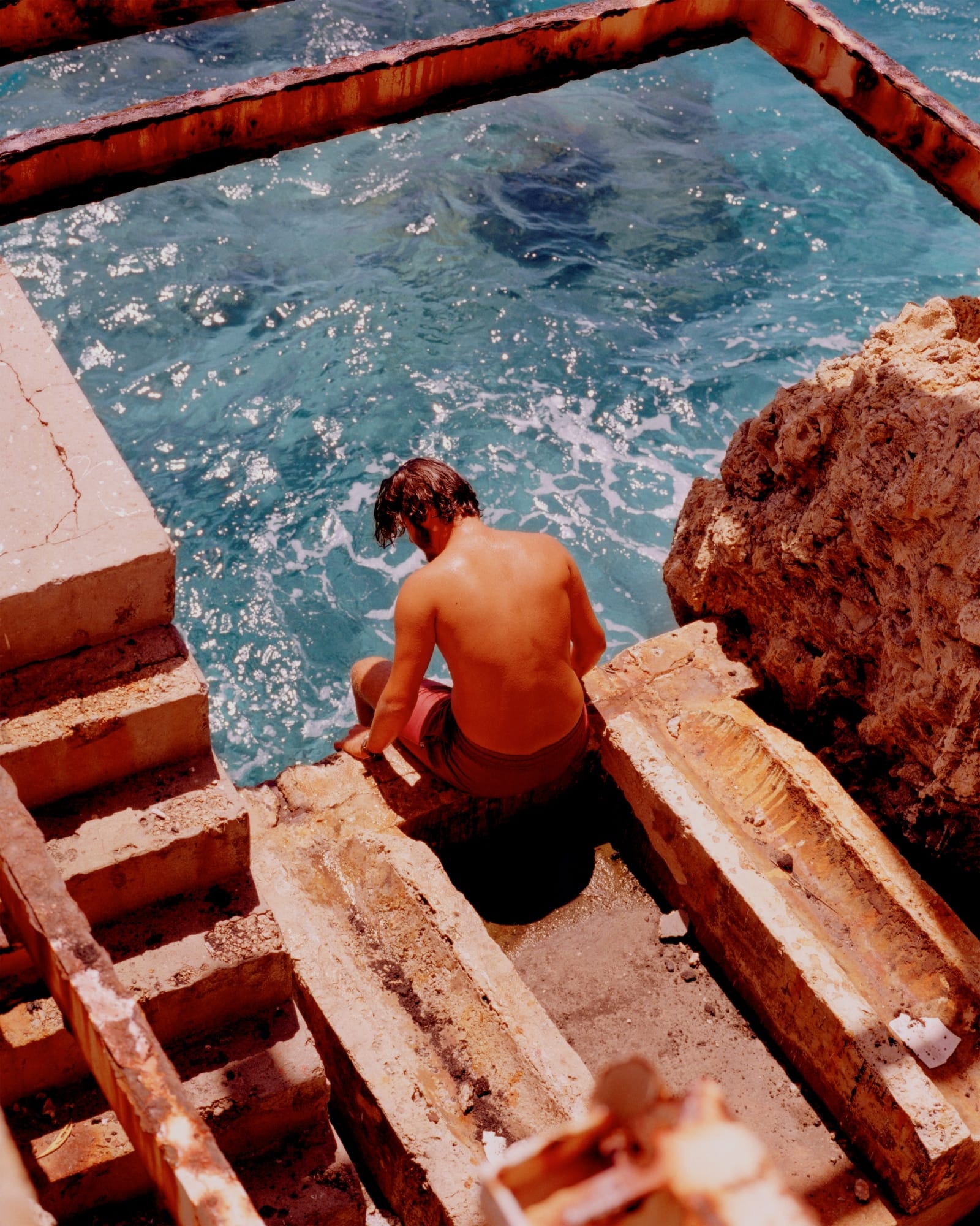 A man in a sunny environment dipping his feet in the ocean.