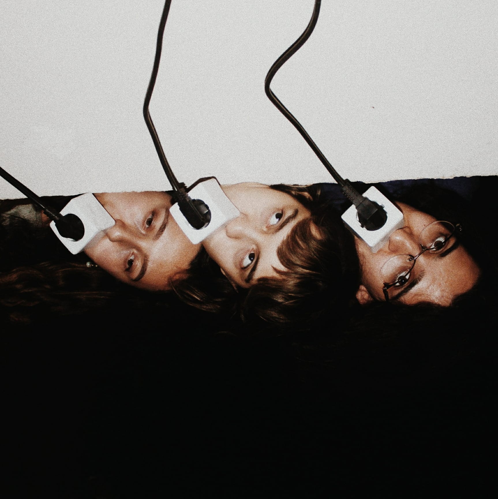Photo of three people showing only their faces, with an electrical plug covering their mouth. © Alp Peker