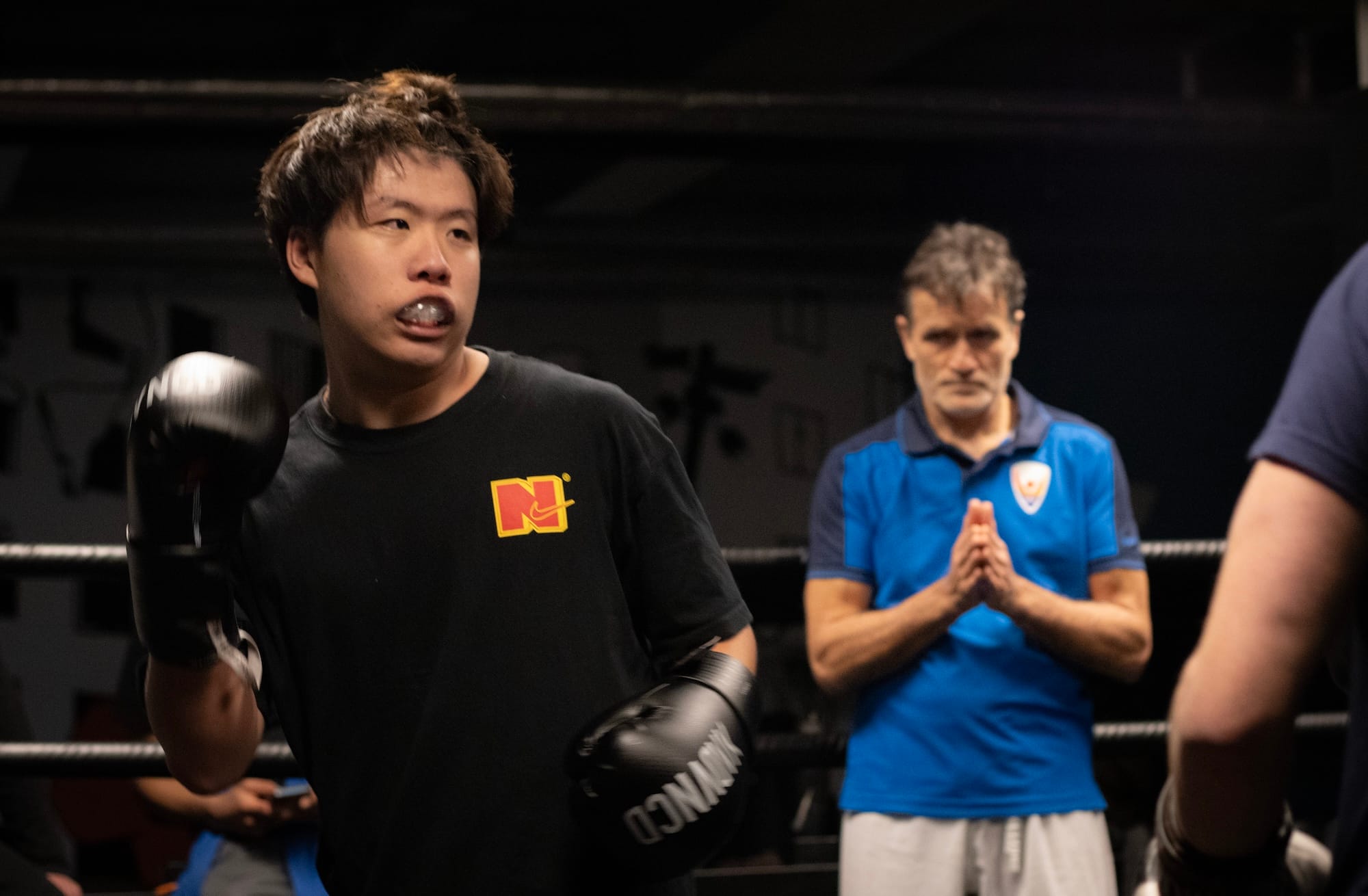 A person in boxing gloves and a black t-shirt, fighting in the ring