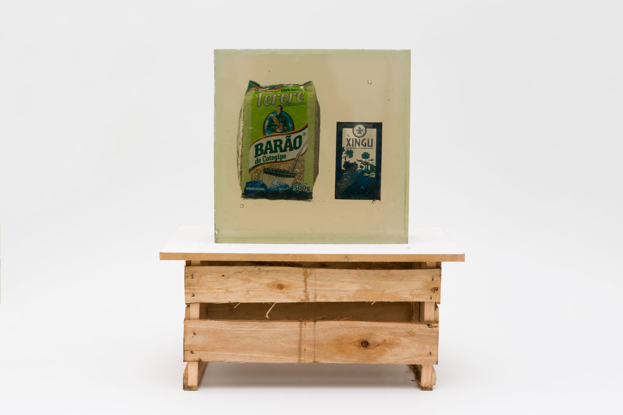 A photograph of a wooden box, with on top two culinary products put into synthetic resin.
