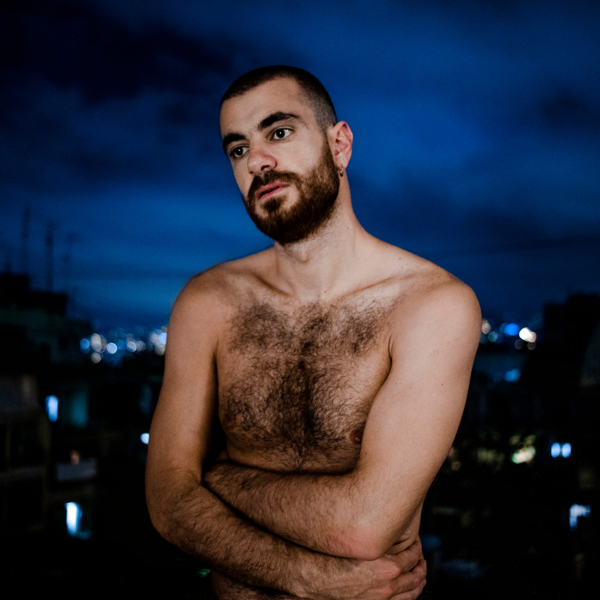 Photograph of a young topless man, staring in the distance with a pensive look on his face.