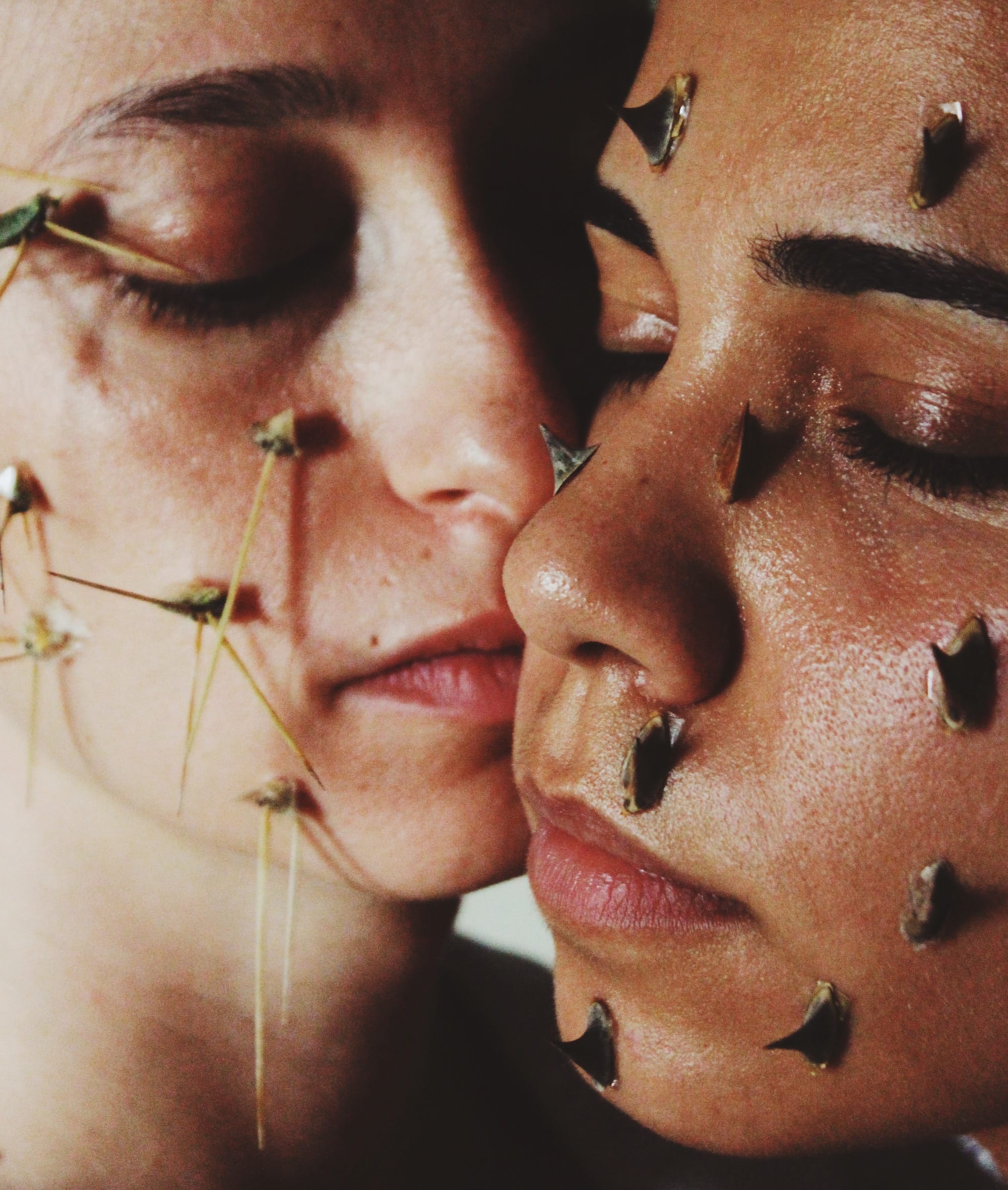 Close-up portrait of two women with their eyes closed, their faces covered with thorns. © Alp Peker