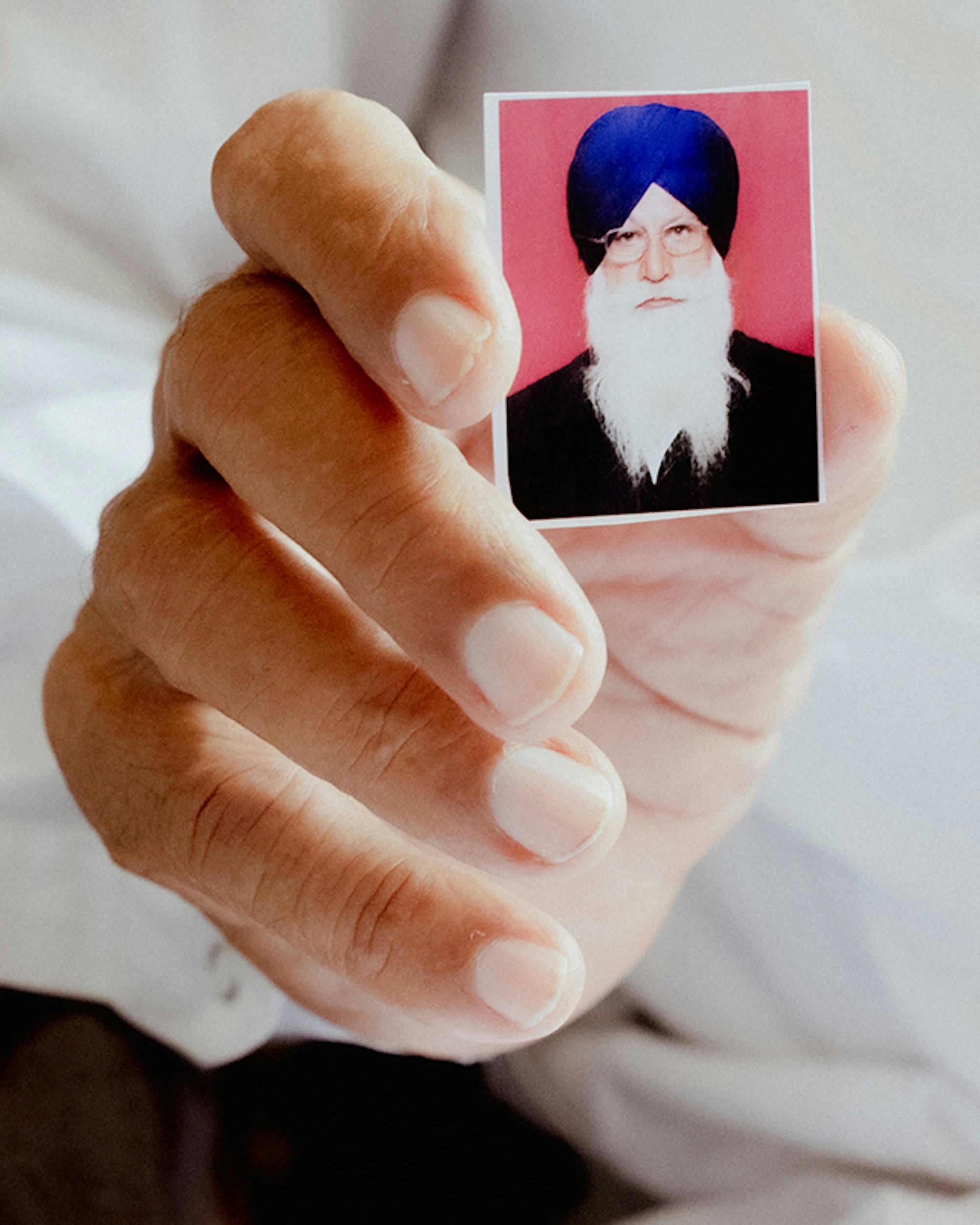 Close-up of a hand showing a passport picture of a bearded man, wearing a dastar (turban)  © Aaryan Sinha