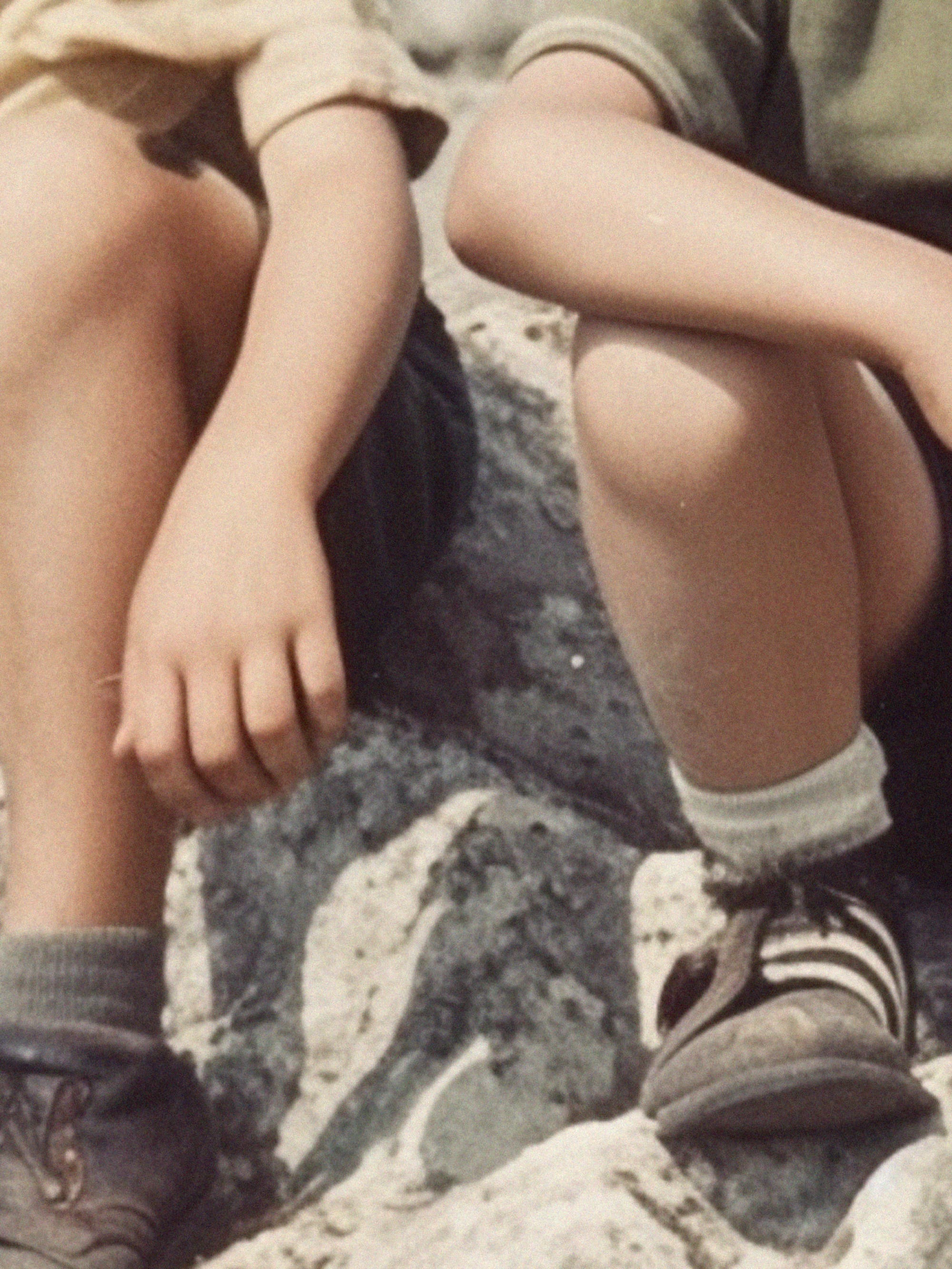 A.I generated image crop of the legs, feet and arms of two white boys sitting on a stony background. © Sander Coers