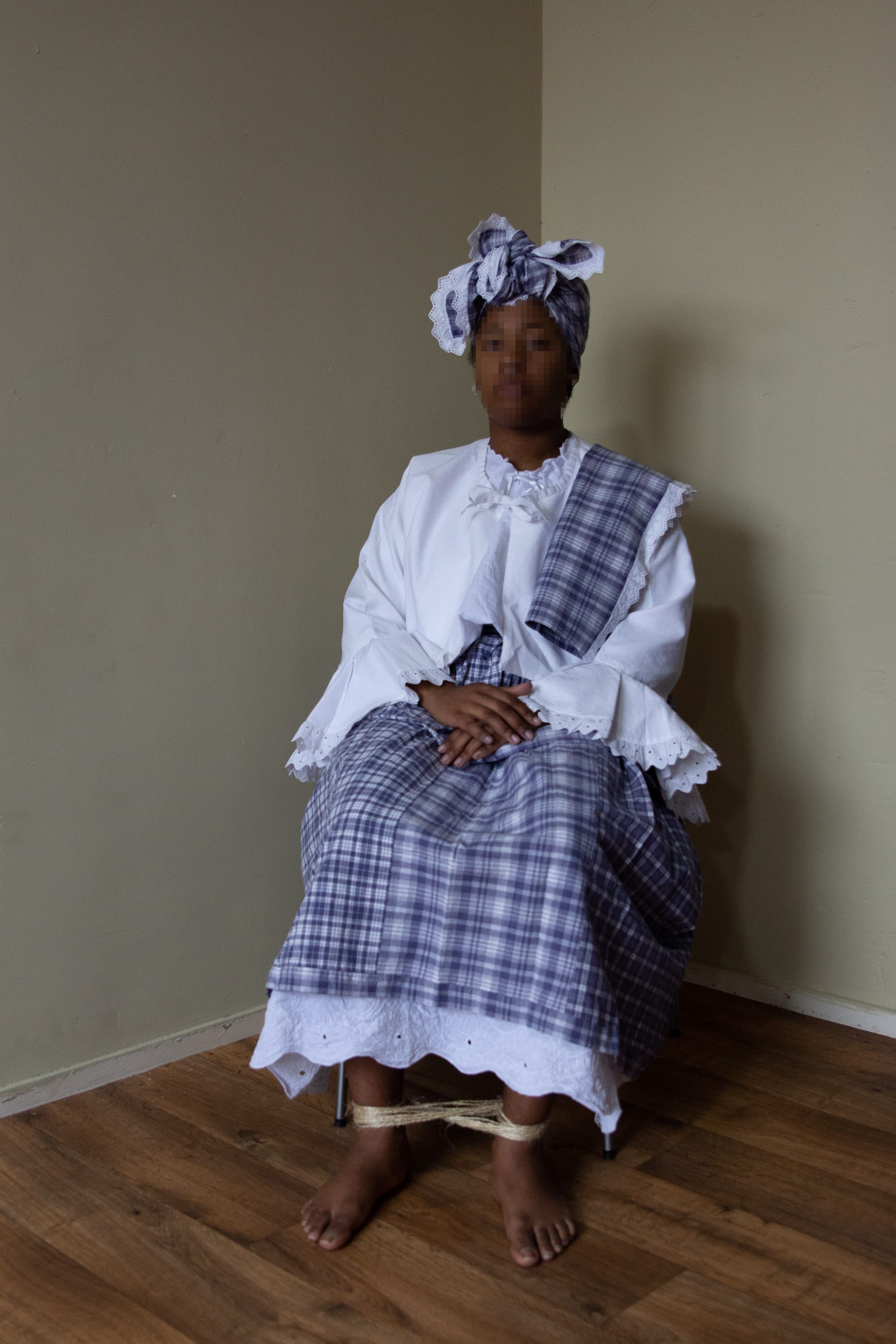 Portrait of a black woman whose feet are tied together, wearing a traditional costume. © Iyanla Etnel