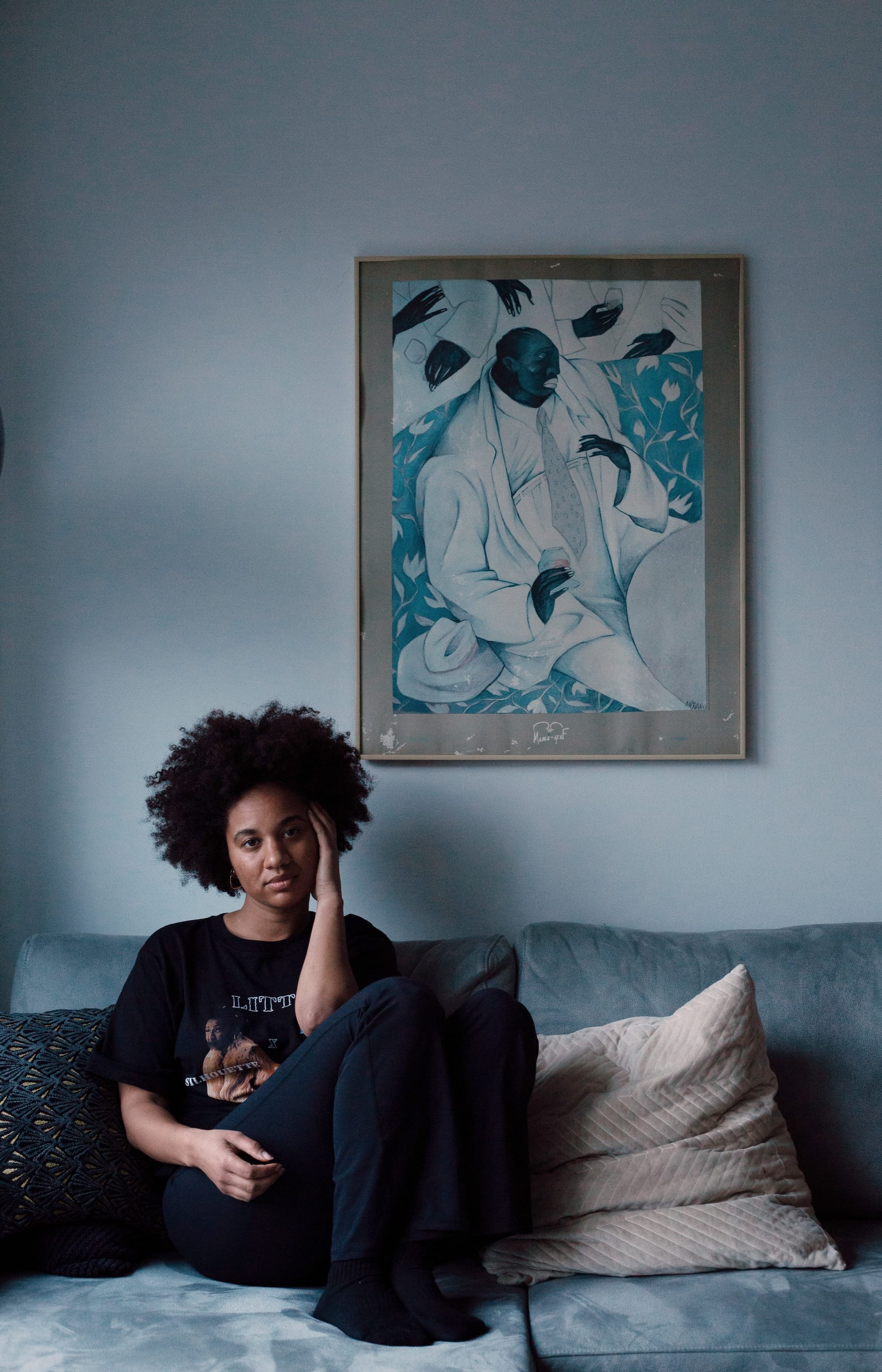 Person sitting on the couch, looking into the camera with a blue painting in the background
