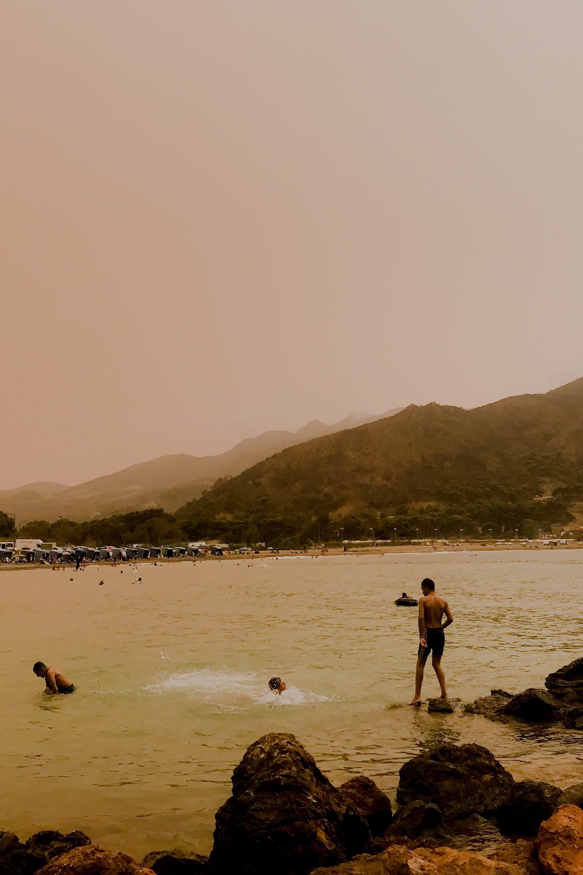 Picture of people on a rocky beach, in soft pink colour tones. © Issam Larkat