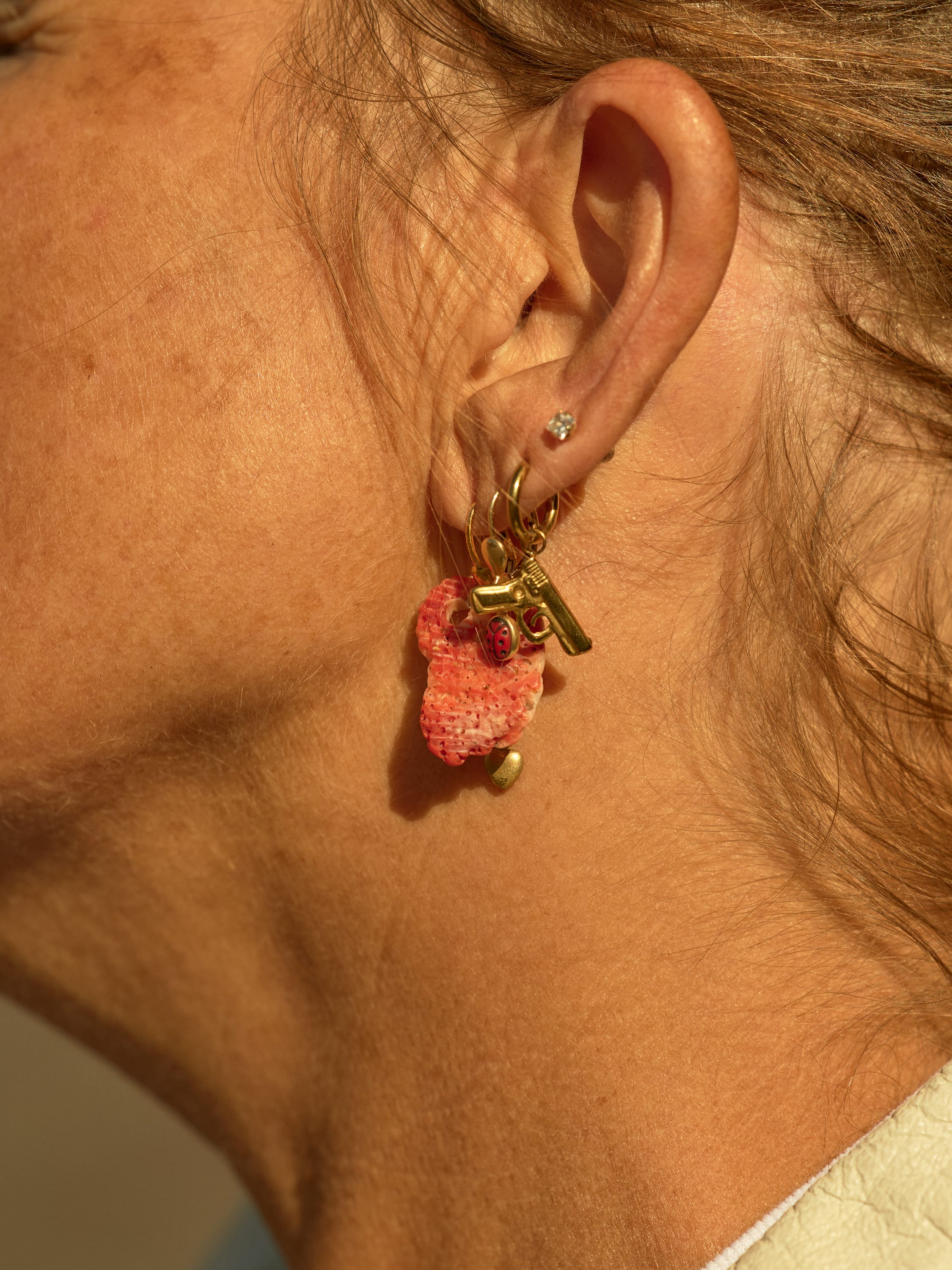 Close-up of a woman's ear adorned with a diamond stud and a gold hoop earring featuring a pink textured charm and a small gold key.