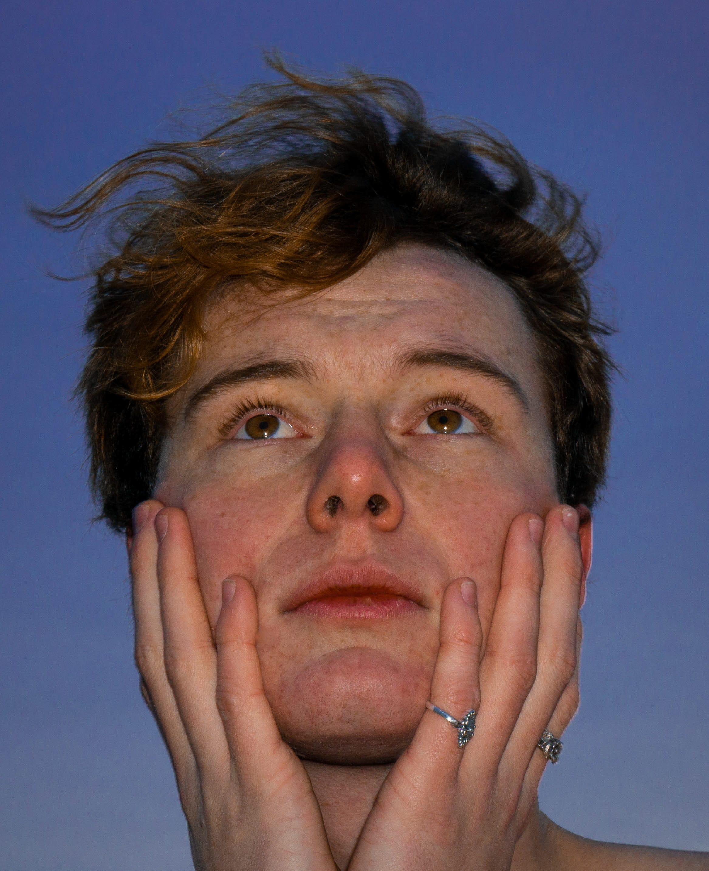 Portrait of a young white man holding his face in his hands. © Tal Ben Yakir