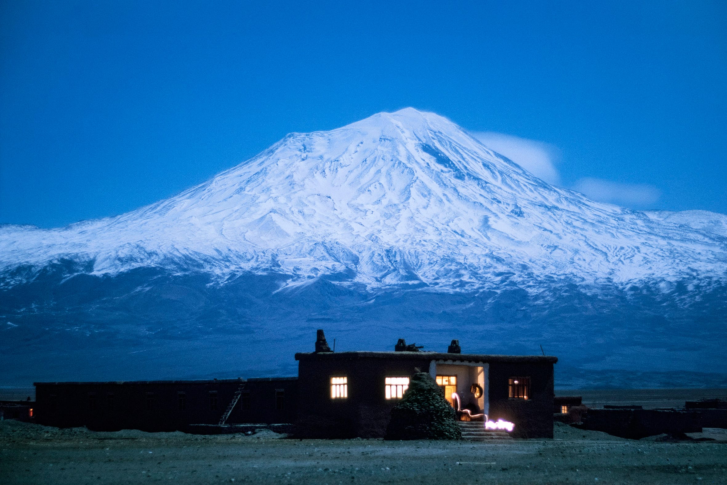 dark house with lights on and snowy mountain in the background