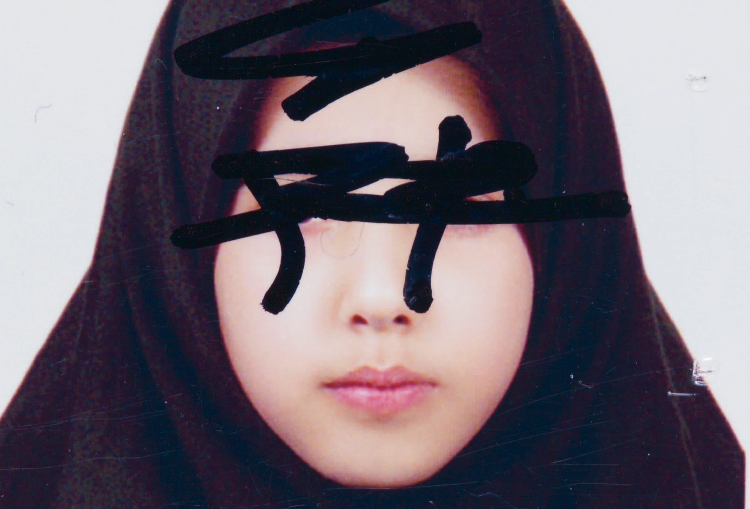 A person wearing a headscarf with their face partially covered by bold black marker strokes.