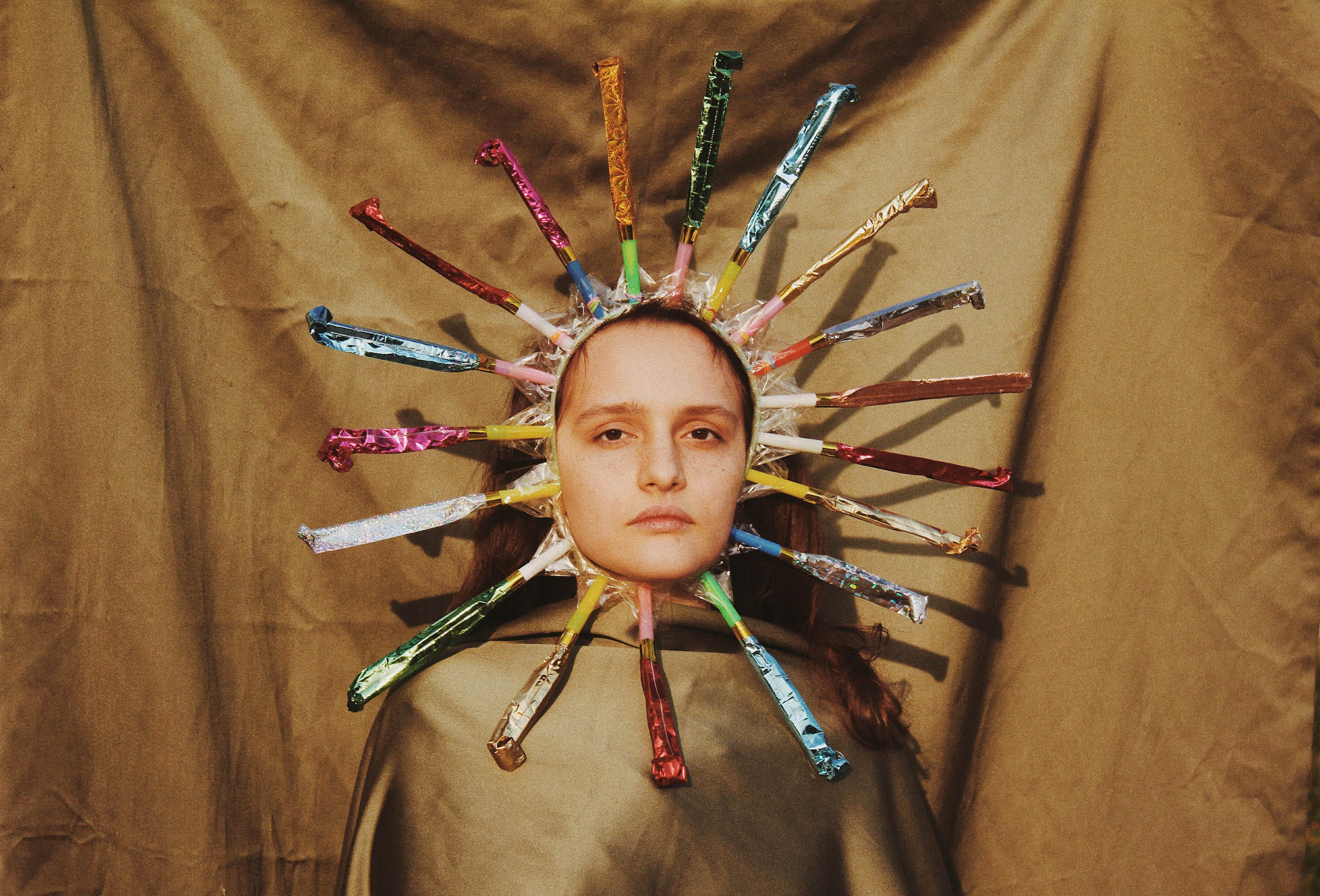 Portrait of a woman in front of a golden fabric, wearing a crown made of party poppers. © Alp Peker