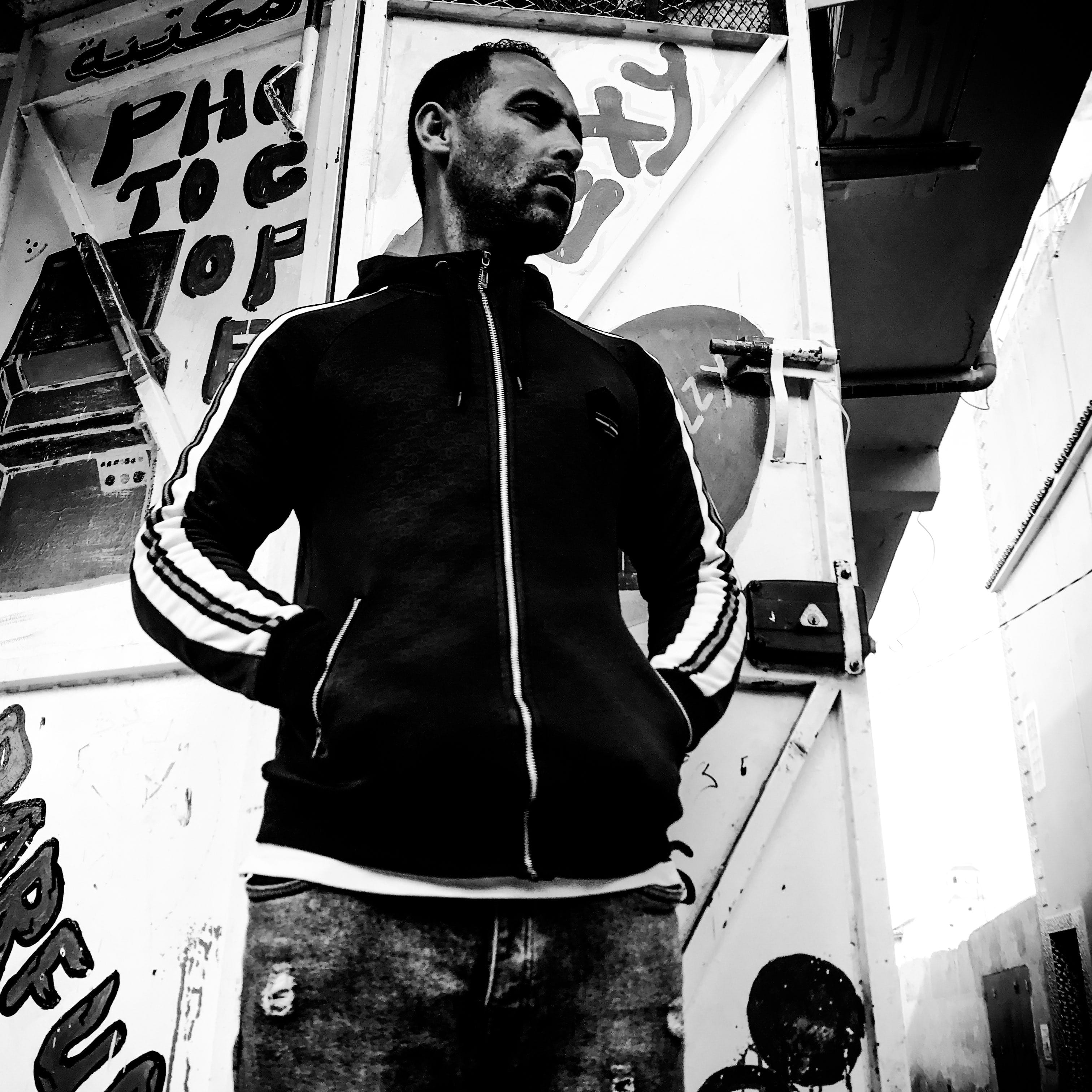 Black and white portrait of a man in front of a steel door with signs. © Issam Larkat