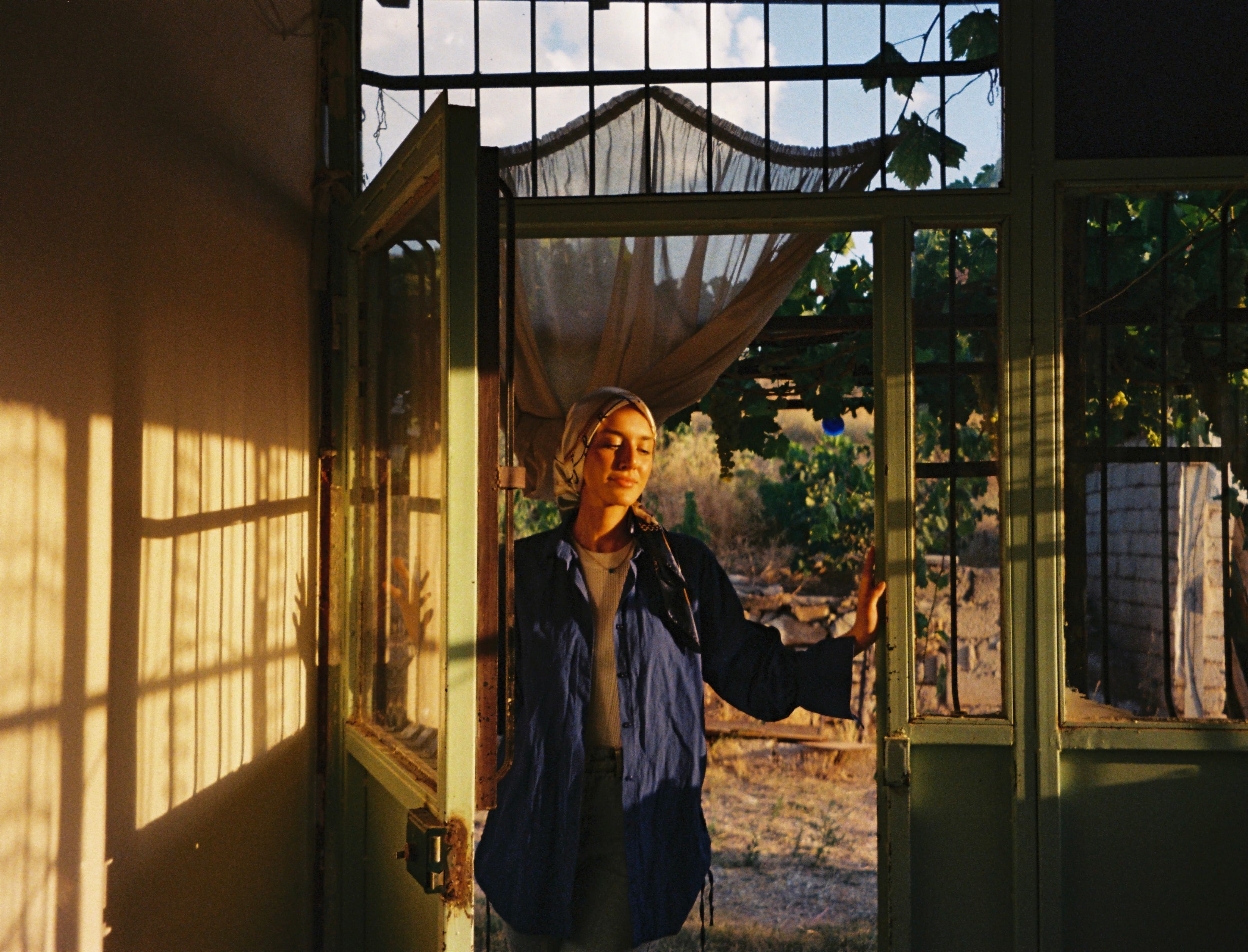 Woman with a headscarf opening the door of a sunny house with many windows
