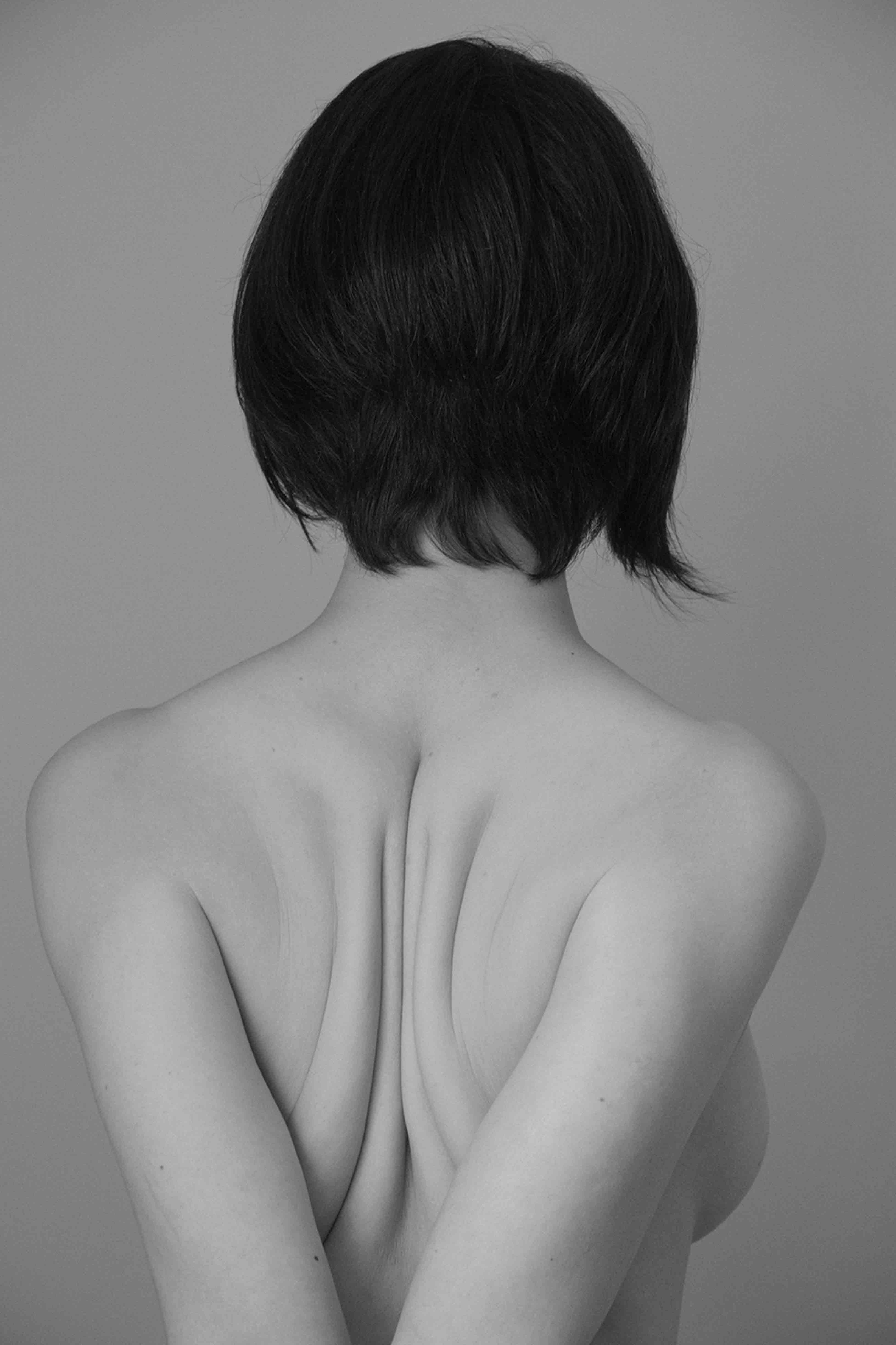 Black and white portrait of the back of a woman, with short black hair, her arms pulled backwards, pushing her shoulder blades together© Marisol Mendez