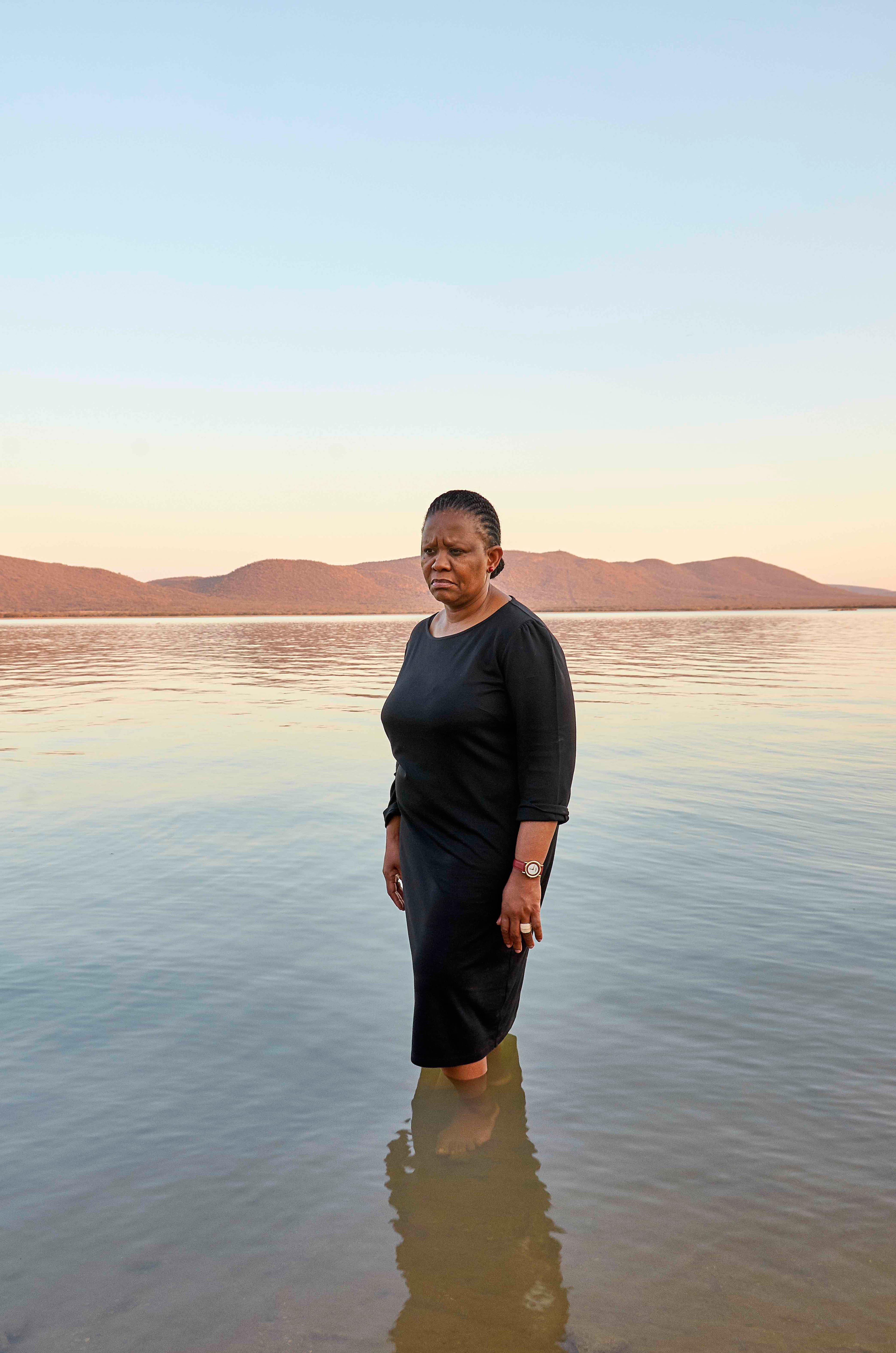Portrait of a Black woman standing in water with mountains in the background. © Thero Makepe