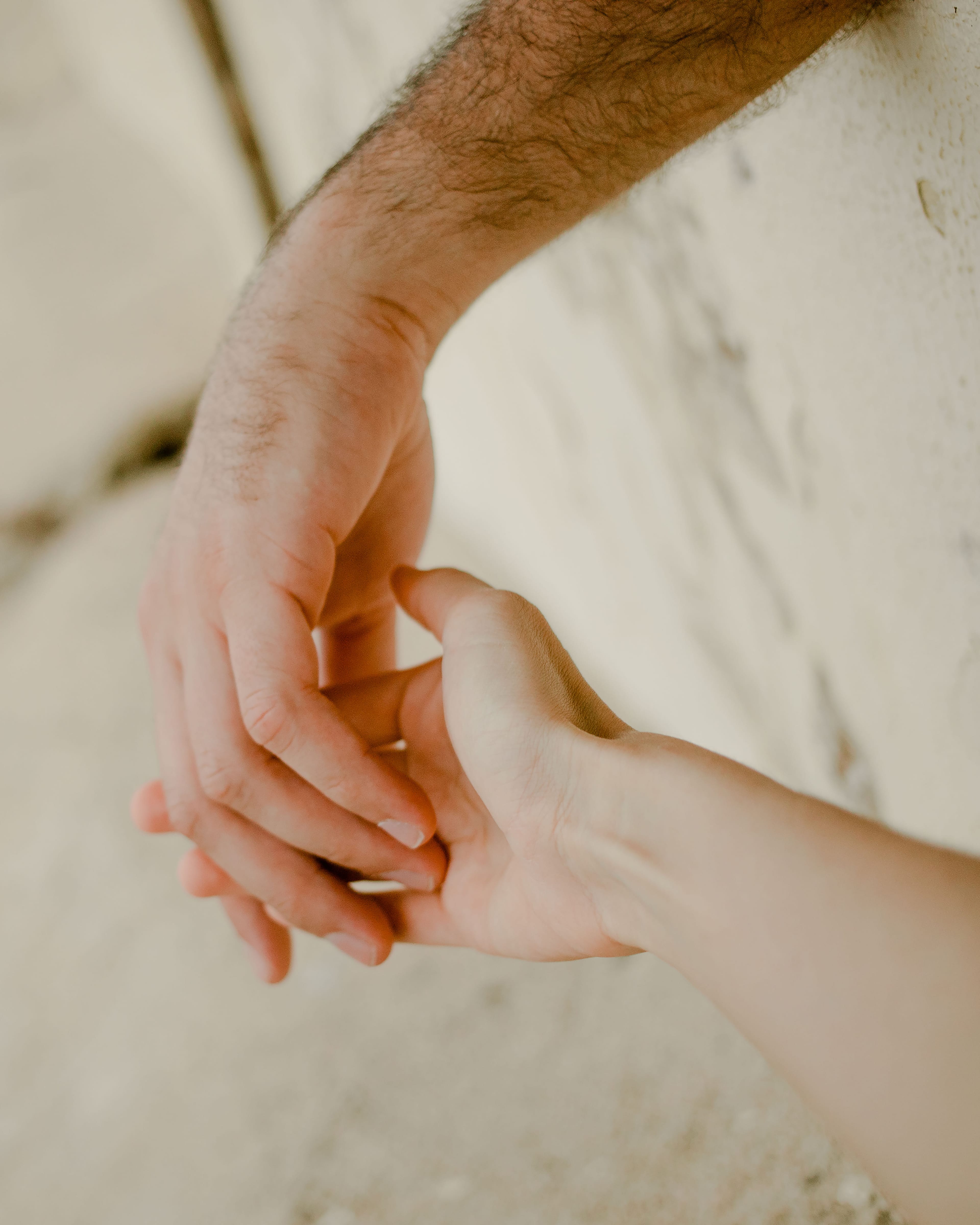 Two hands gently holding each other against a blurred, light-colored background, conveying a sense of connection and tenderness.