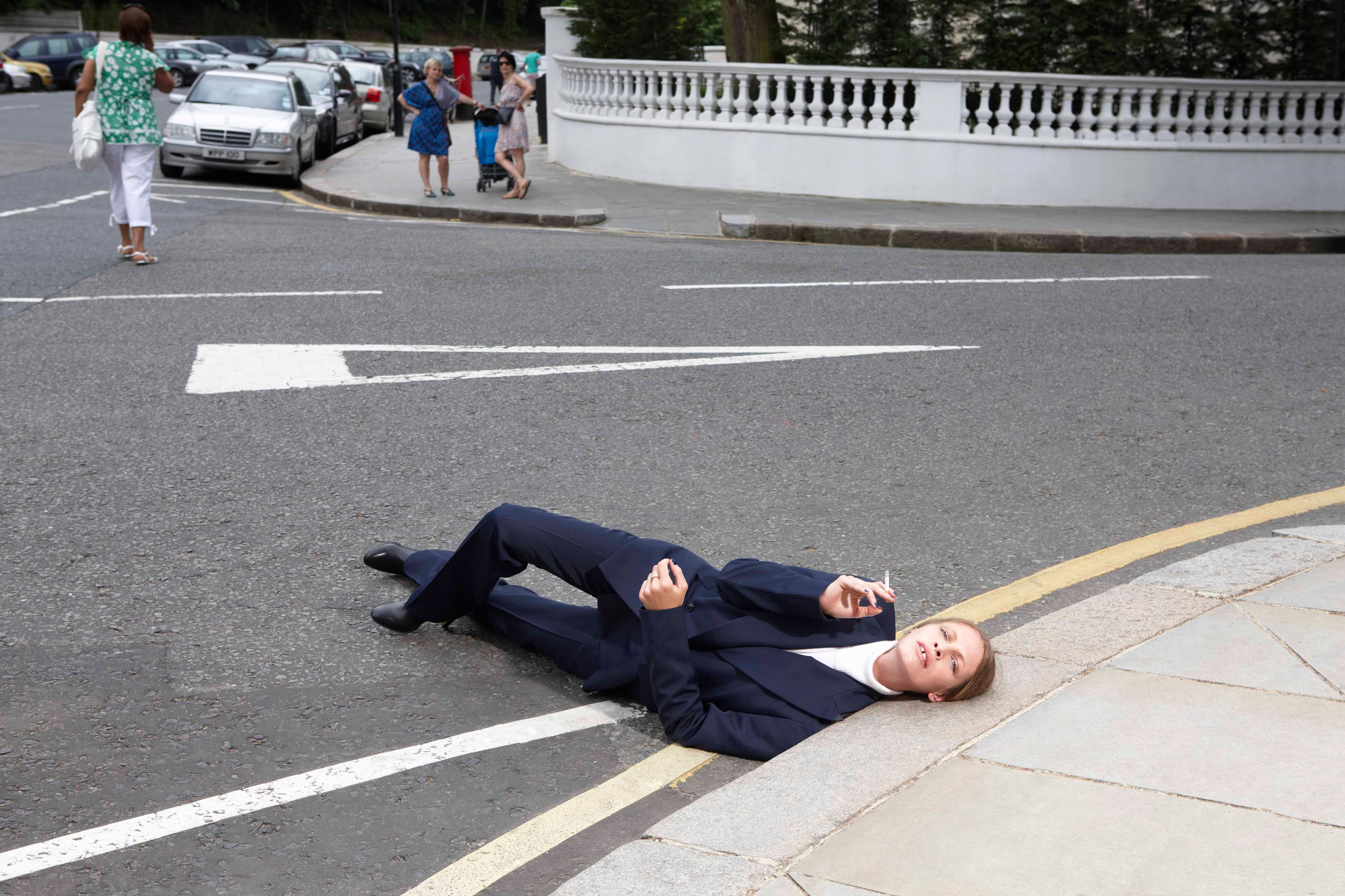 woman smoking on the floor with head on side walk wearing suit