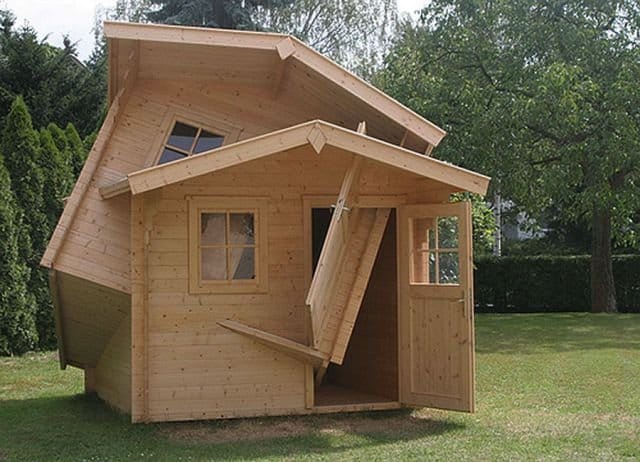 Two identical wooden sheds in a garden, collapsed together in a glitch