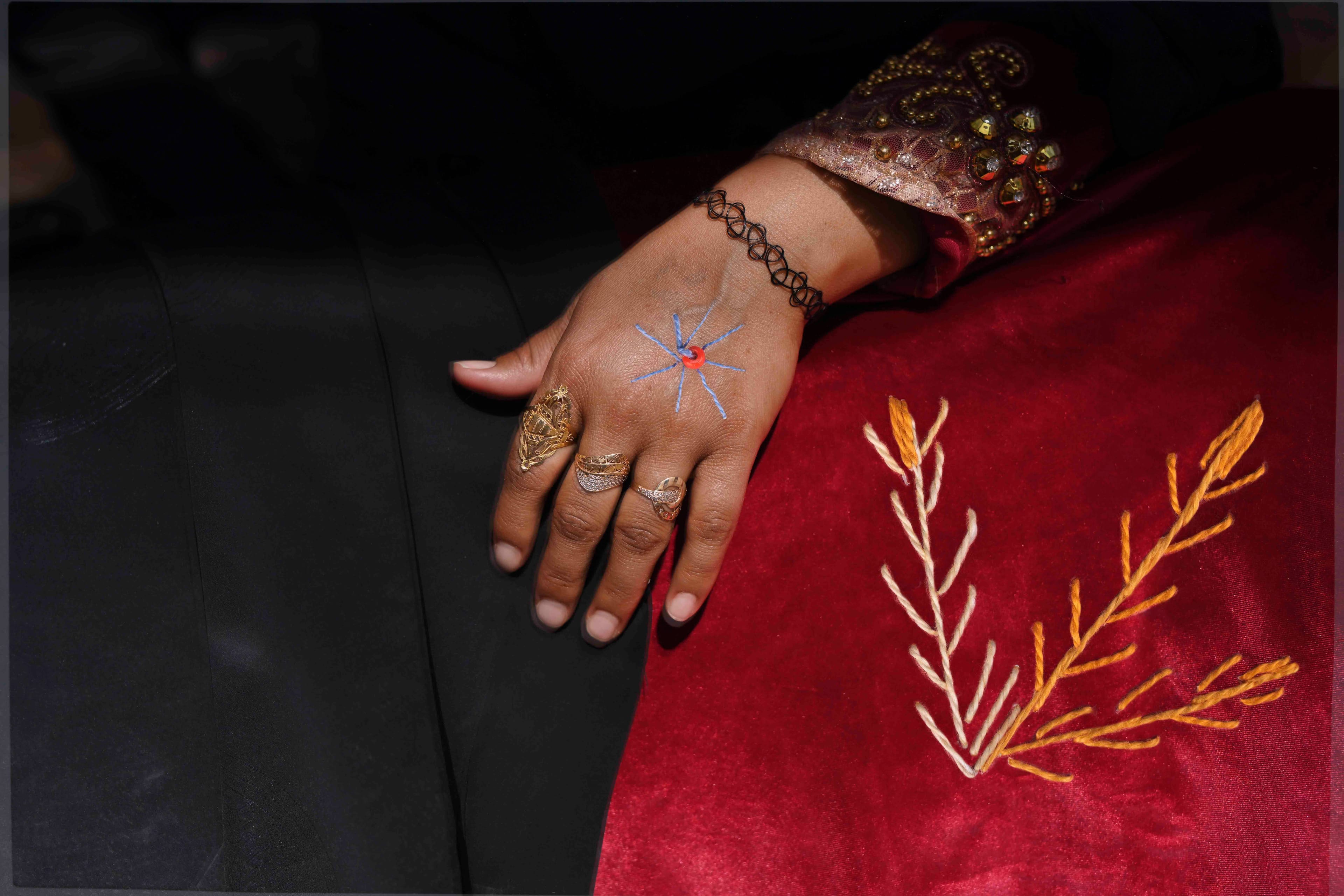 Close-up of a woman's hand, with bracelet and rings. Some geometric embroidering is covering her skirt and hand© Rehab Eldalil