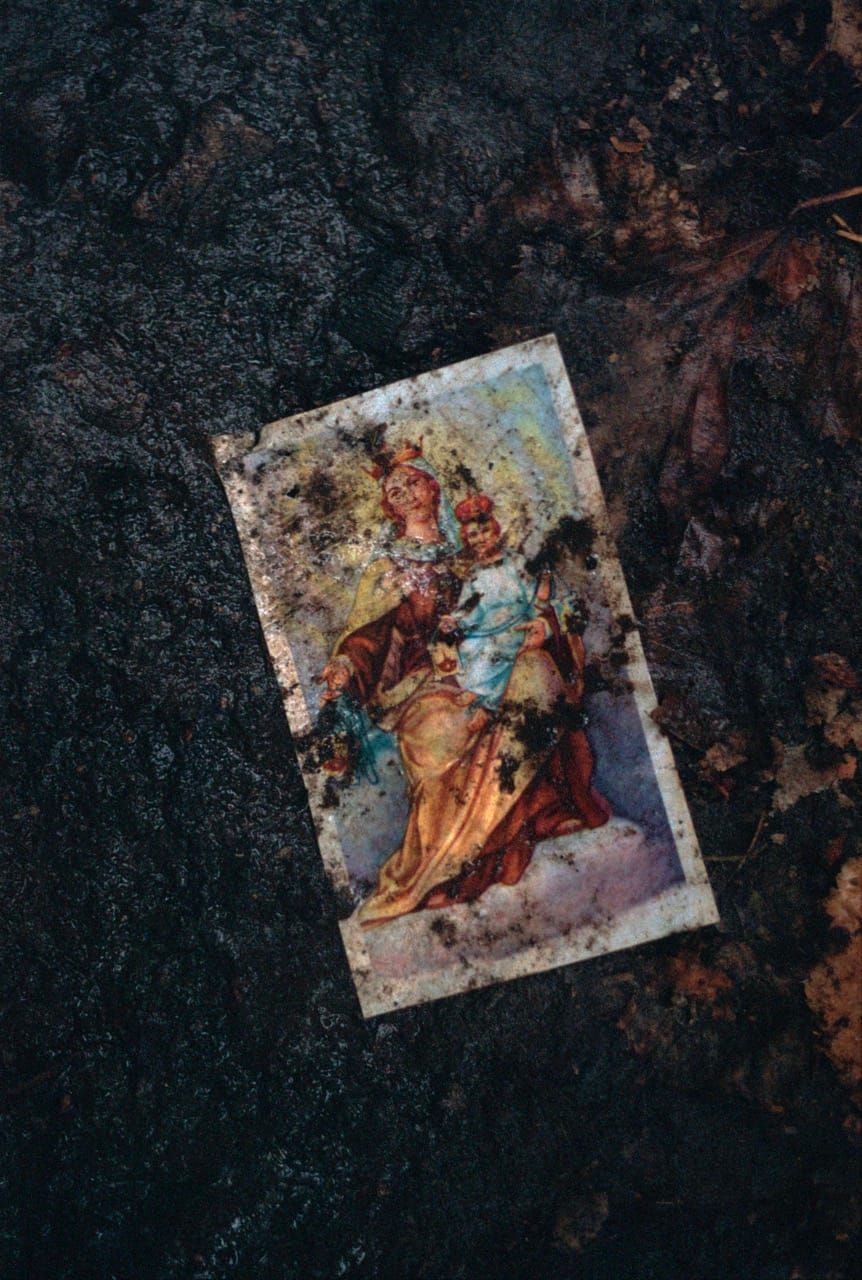 A weathered, colorful image of two figures in ornate clothing lies on dark, muddy ground, partially covered in dirt and debris.