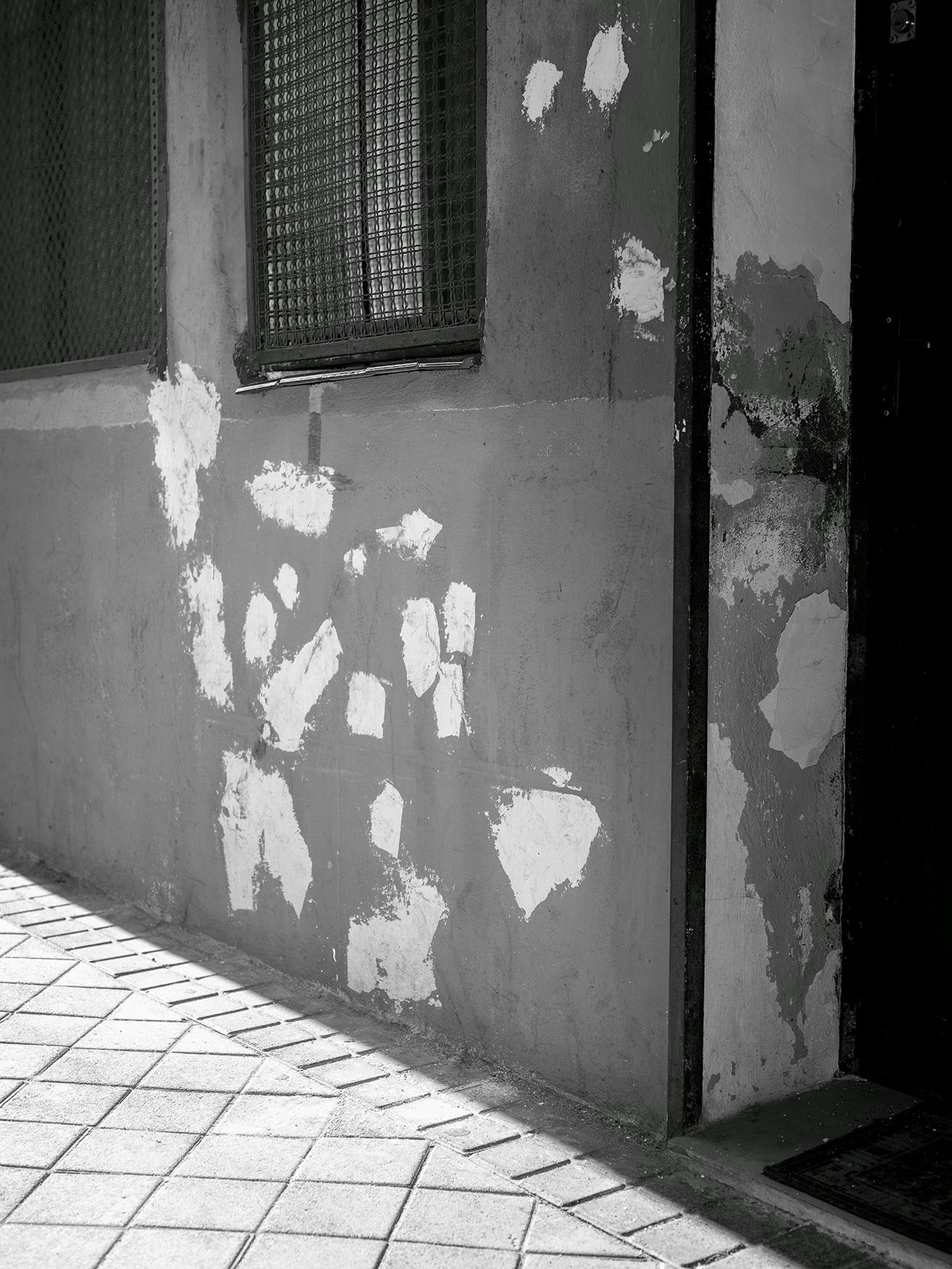Black and white image of a shrapnel-scarred facade of a house. The bullet holes are plastered over. © Bebe Blanco Agterberg
