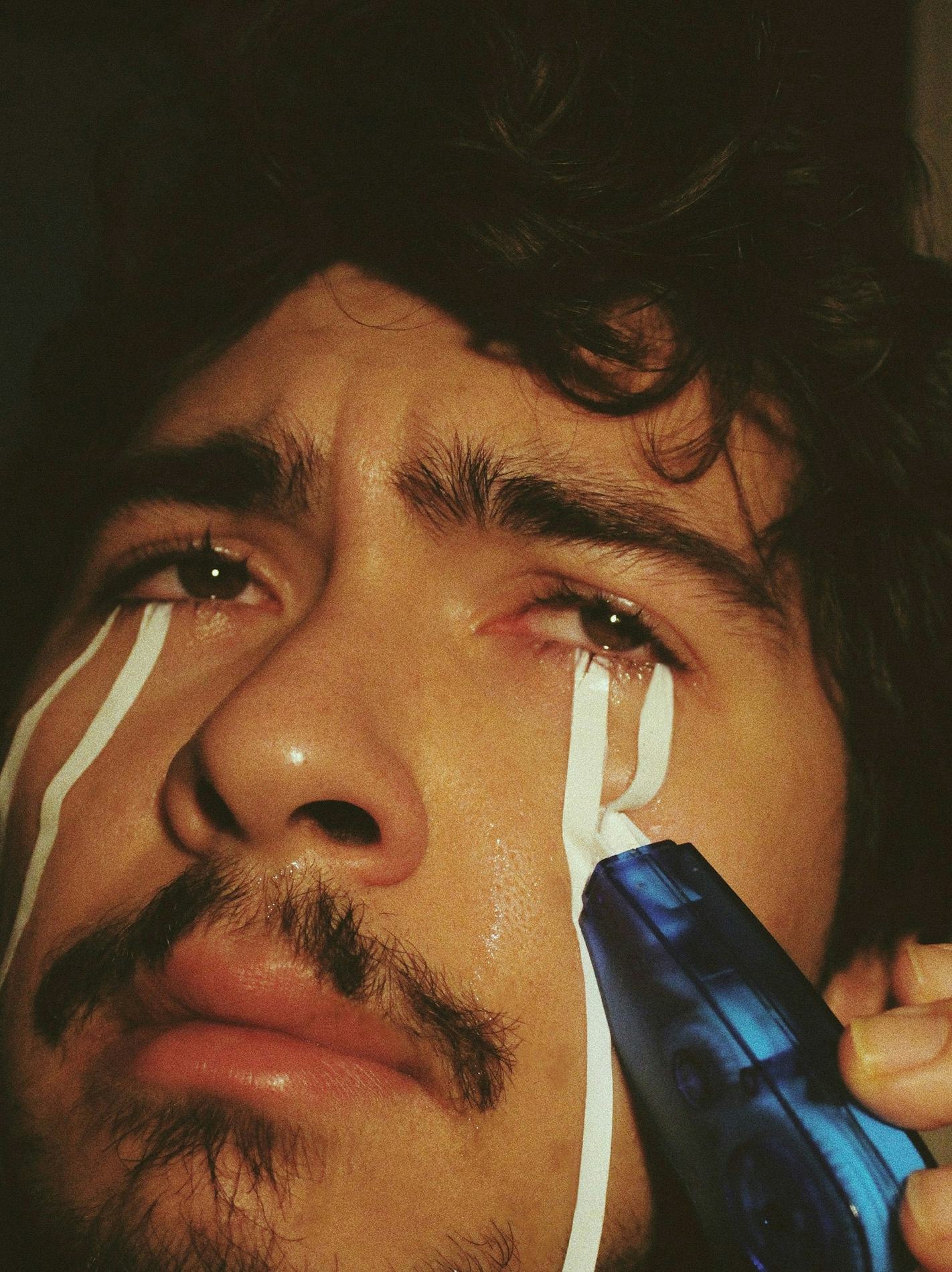 Self portrait of Alp Peker crying, whilst rolling correction tape over his cheeks. © Alp Peker
