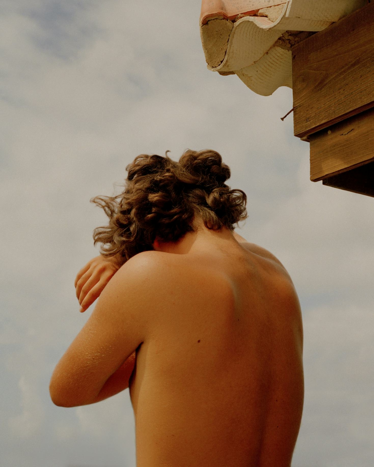 A young boy with his back turned to the camera, covering his head in his arms.