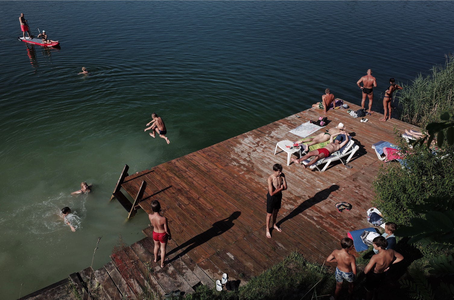 people swimming and tanning at wooden platform by a lake