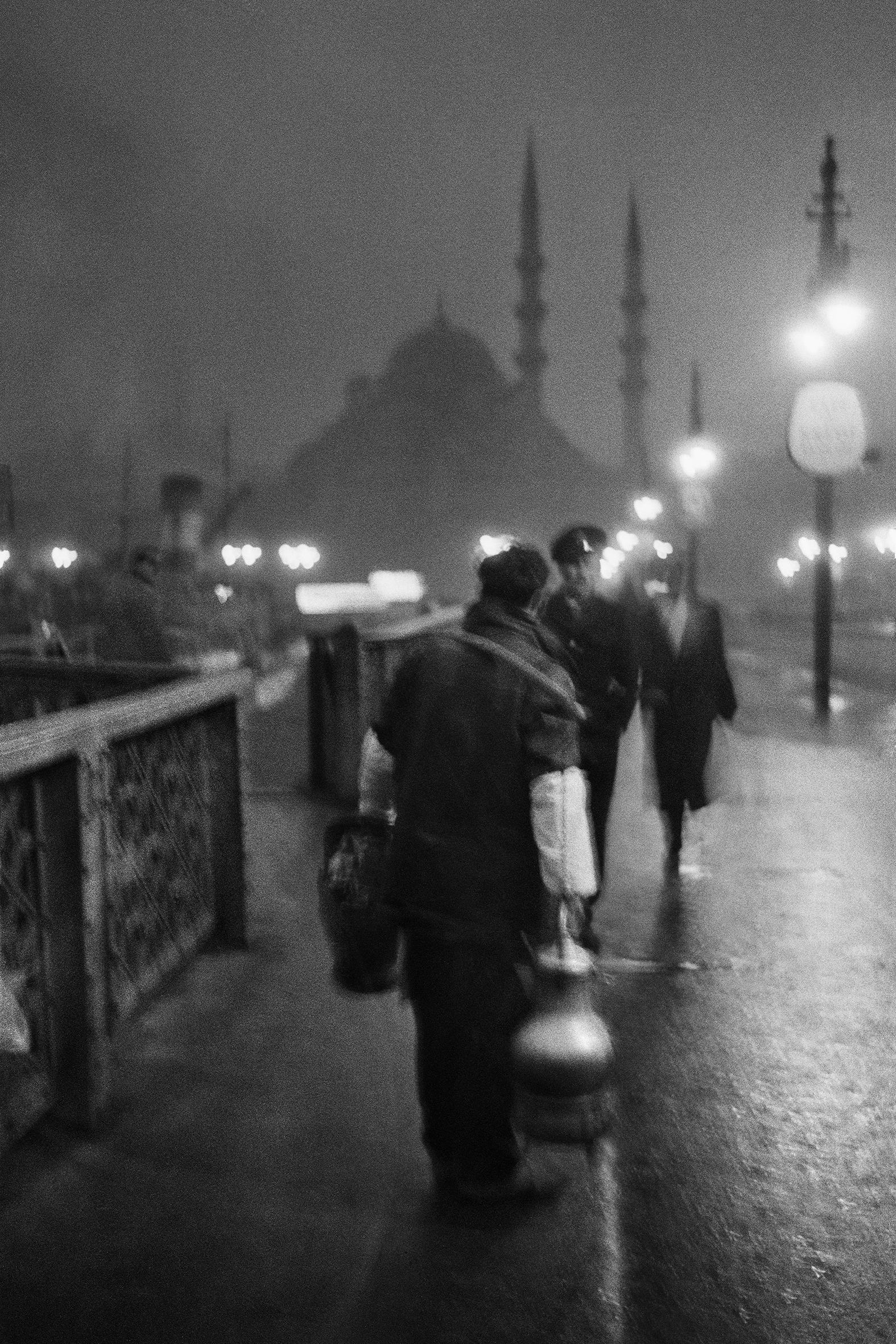 Black and white image of a street vendor at night on the Old Galata Bridge, in Istanbul. © Ara Güler