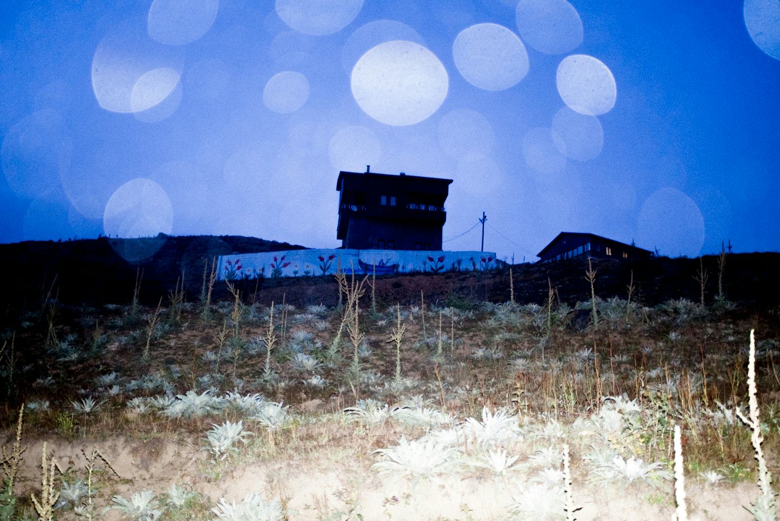 Photo of a house in the Kushmer Highlands in Turkey at night, with flash. The flash lights up the blue night sky. © Cansu Yıldıran