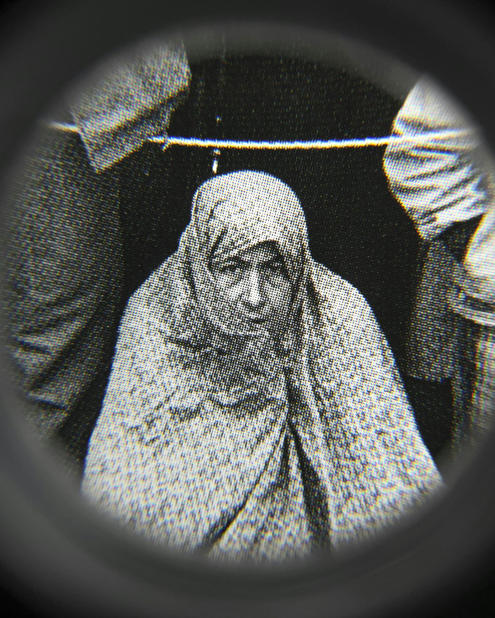 Black and white close-up image of an existing photograph, showing a woman wearing a chador, staring into the camera. Shot through a magnifying lens © Amin Yousefi