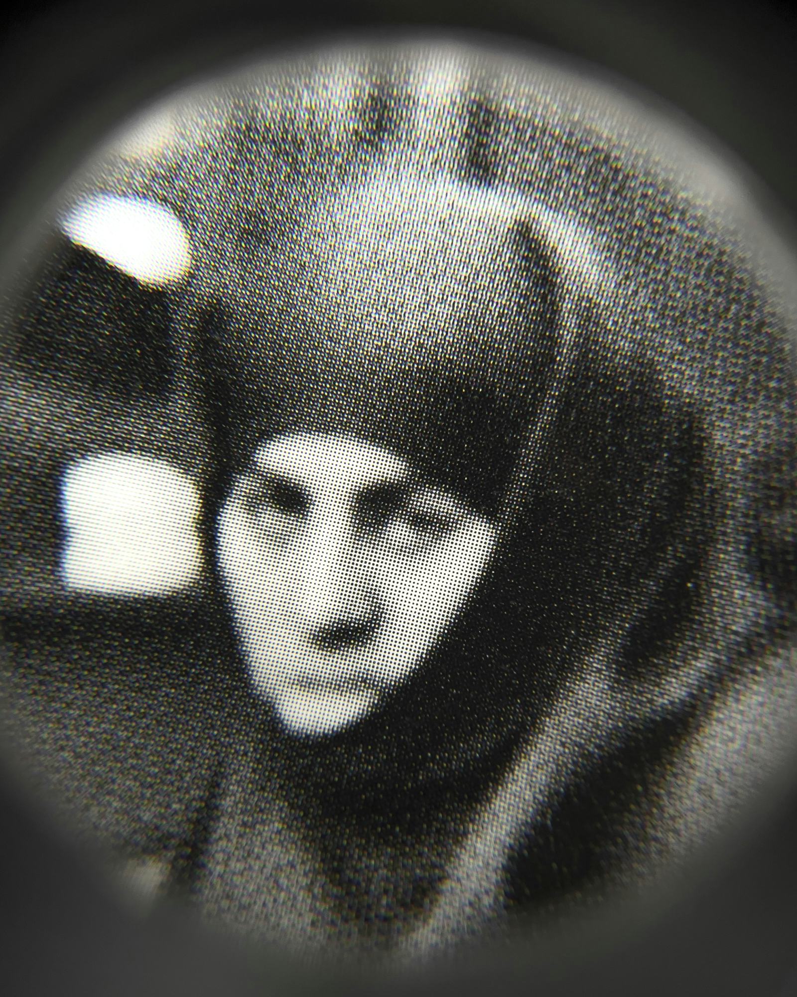 Black and white close-up image of an existing photograph, showing a woman wearing a chador, staring into the camera. Shot through a magnifying lens © Amin Yousefi