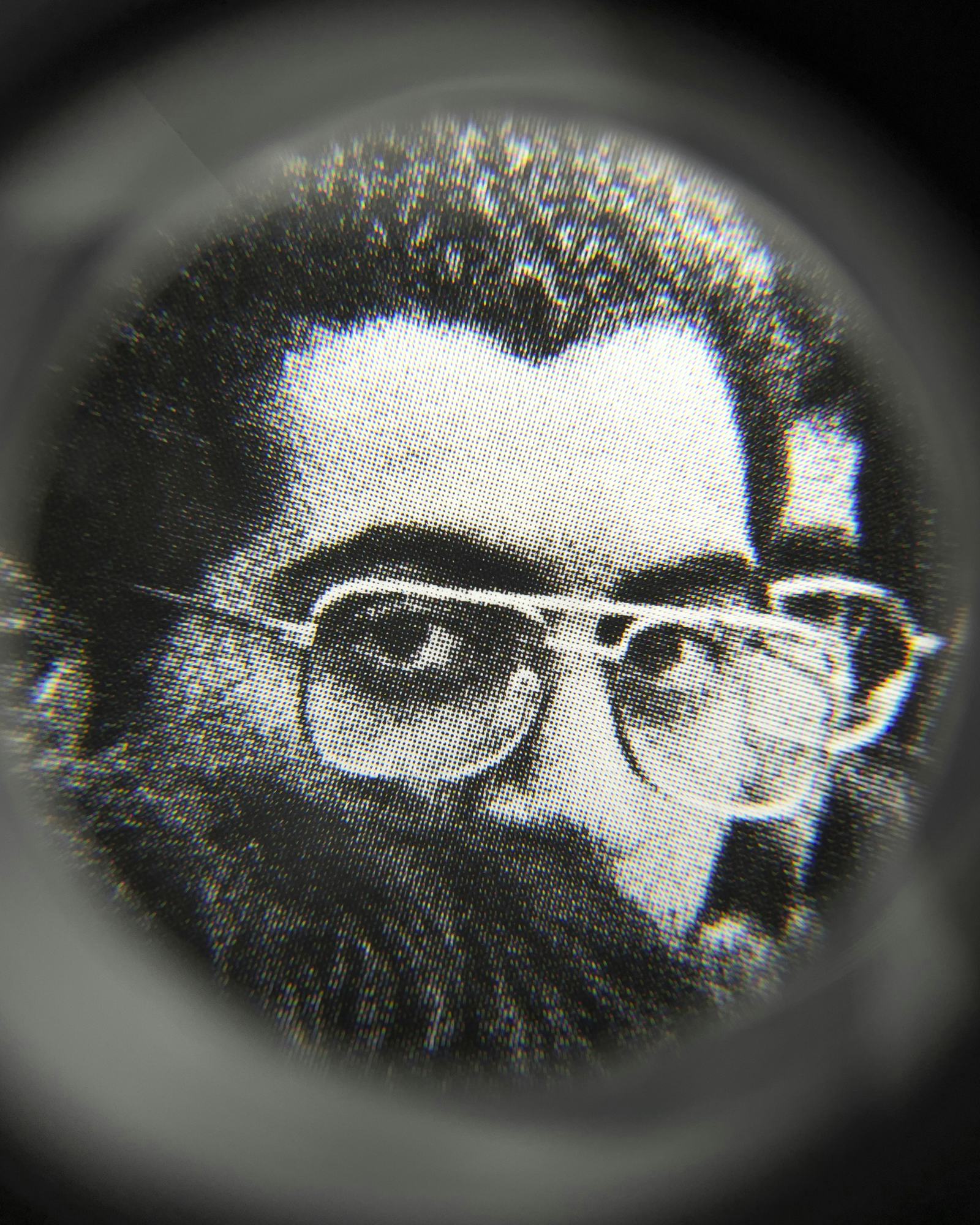 Black and white close-up image of an existing photograph, showing a man staring straight into the camera. Shot through a magnifying lens © Amin Yousefi
