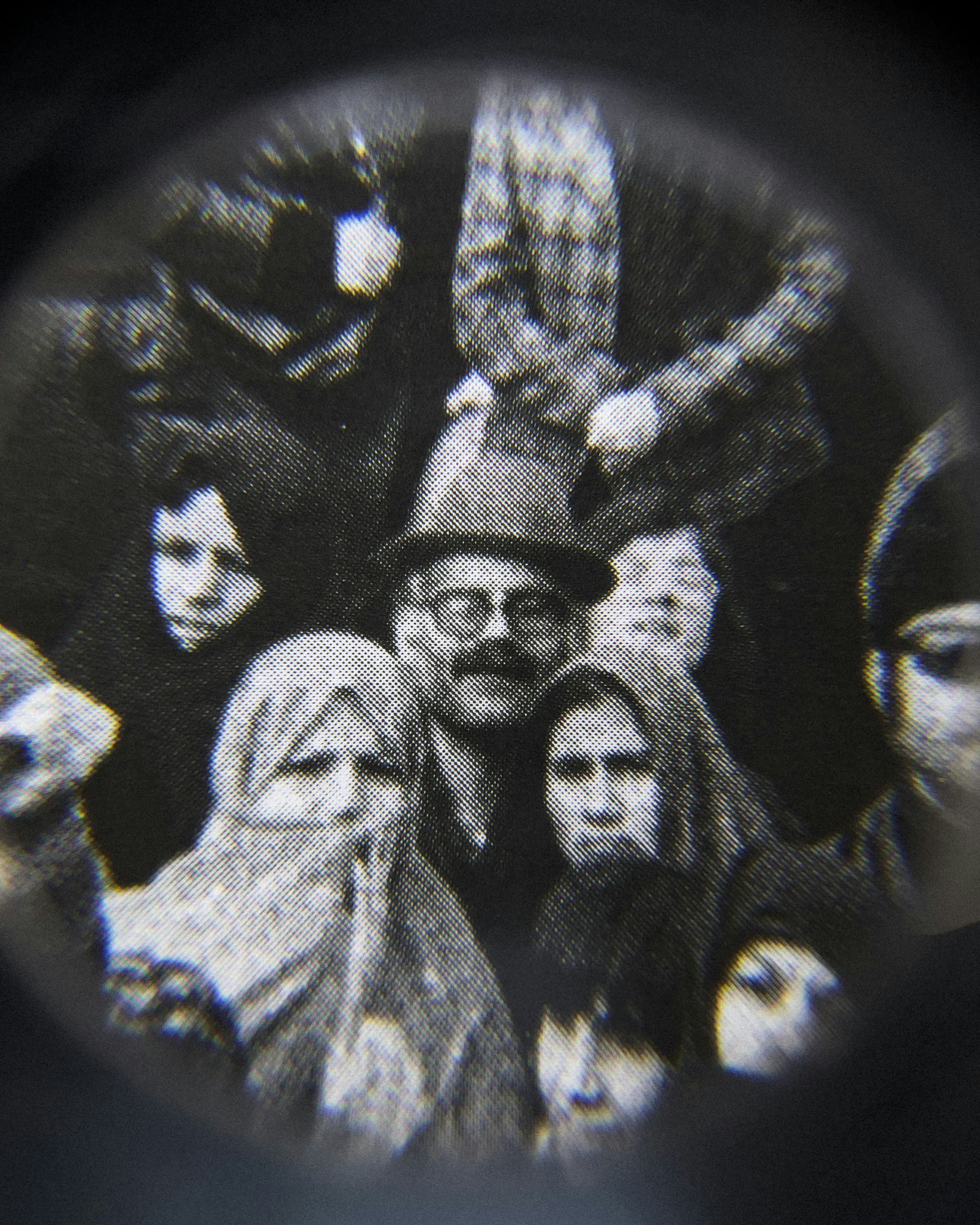 Black and white close-up image of an existing photograph, showing several people in a crowd staring into the camera. Shot through a magnifying lens © Amin Yousefi© Amin Yousefi