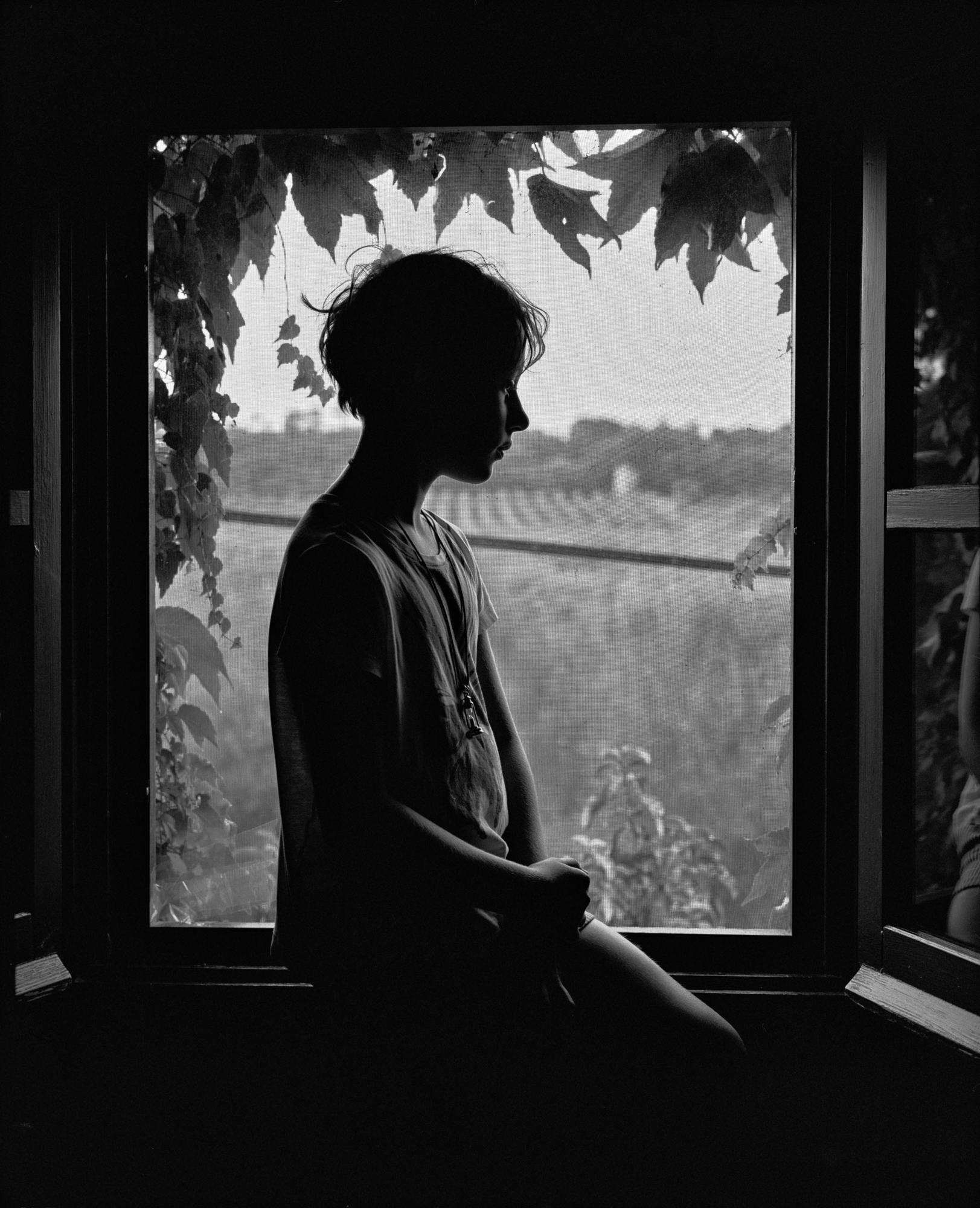 Black and white photograph of child sitting in window sill