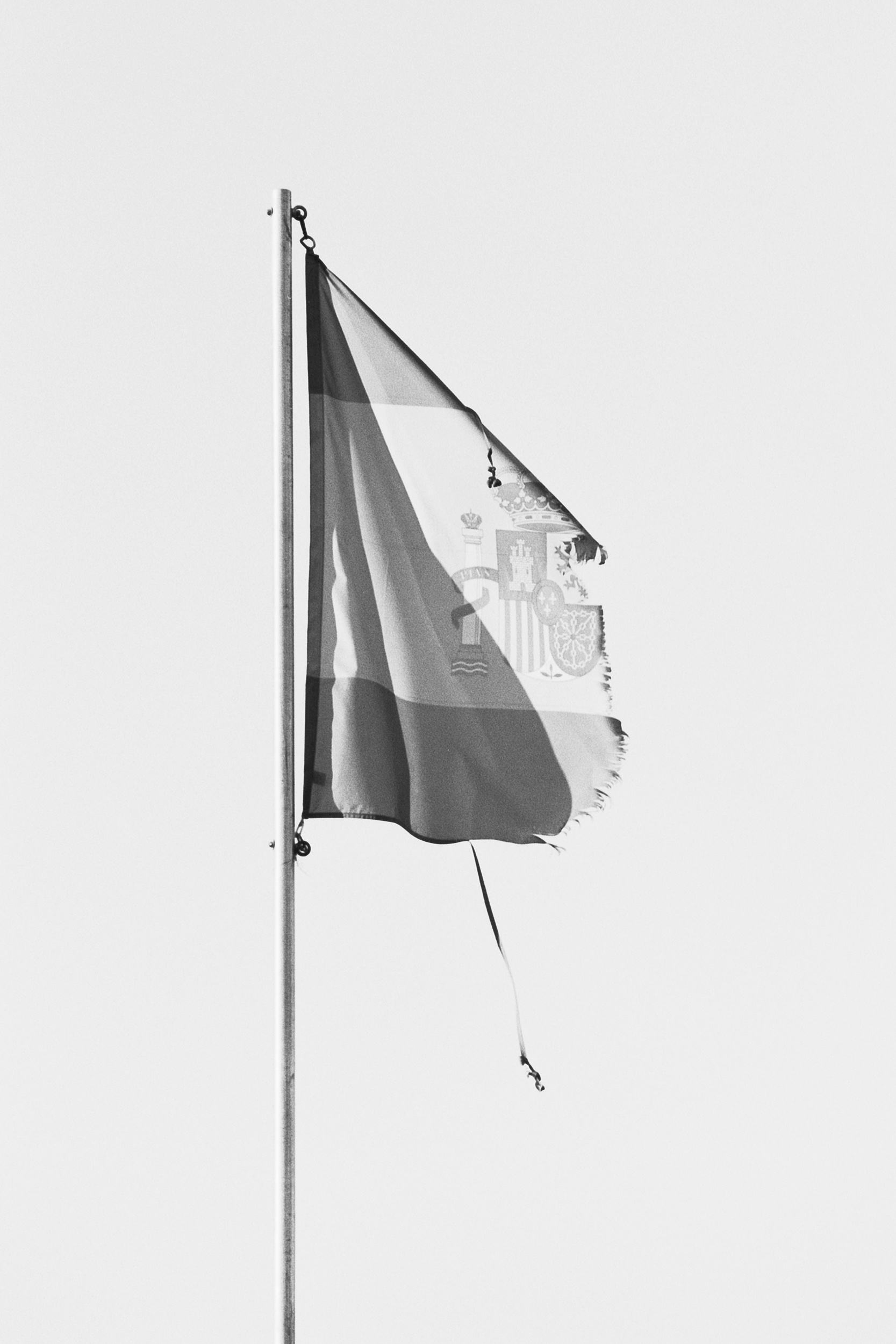 Black and white image of a Franco-era flag on a flag pole. The flag is torn and only one half remains. © Ignacio Navas