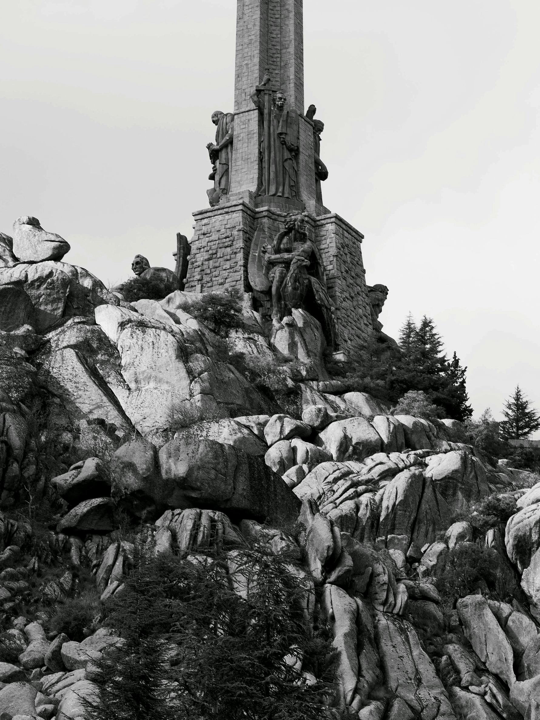 Black and white image of a rocky environment, in the Valley of the Fallen (Spain). The base of a large monument with statues is visible. © Bebe Blanco Agterberg