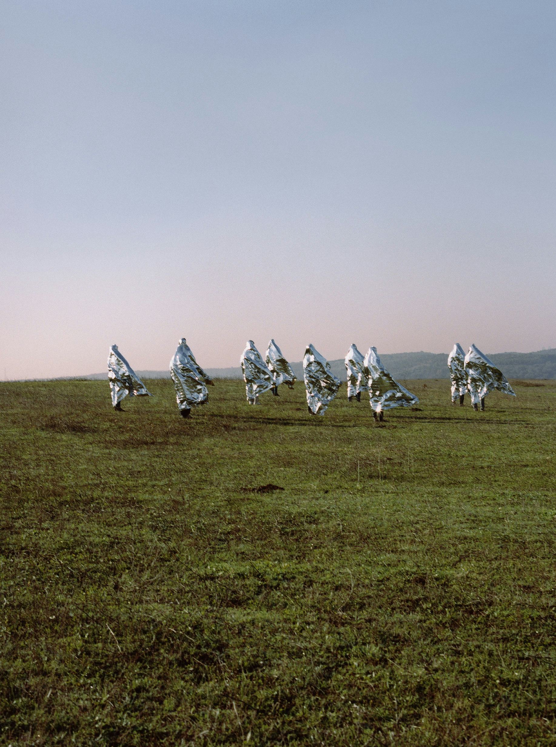 group of people standing in field with pink sky and metallic covers