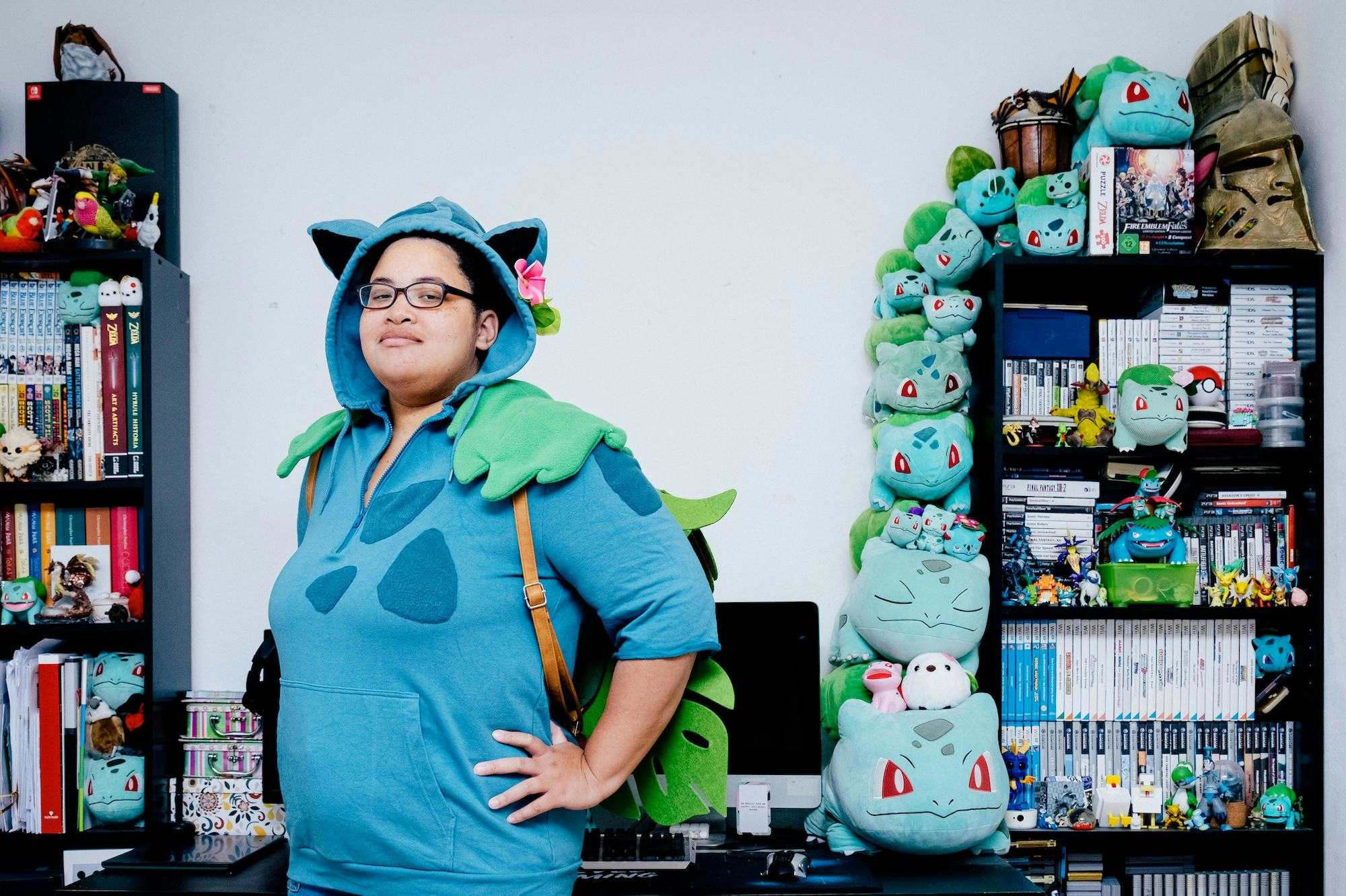 Person proudly posing in the bedroom with many Bulbasaur figures stacked behind