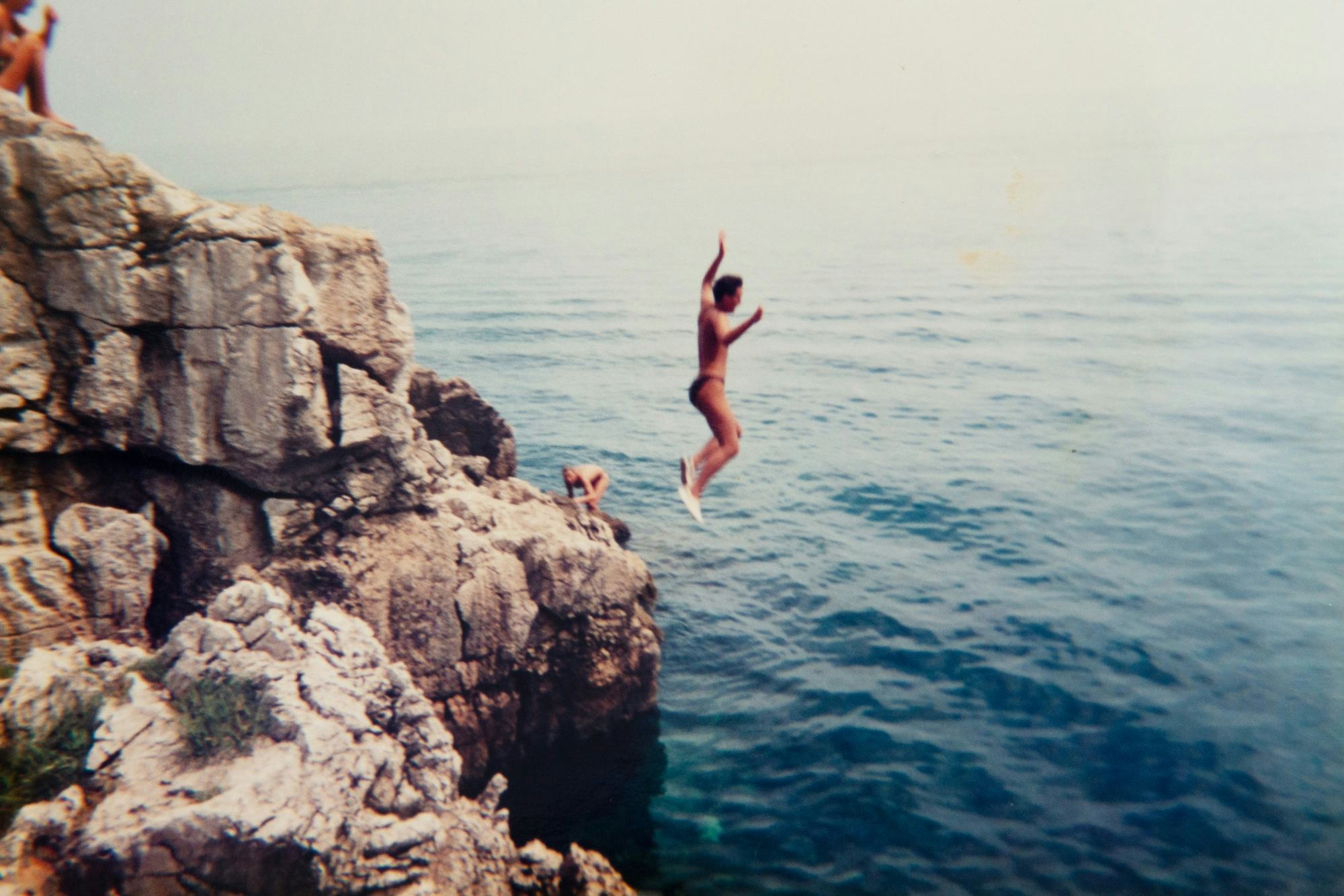 Archival holiday picture from the artist's personal archive, showing swimmers jumping into the ocean from a rock formation© Sander Coers
