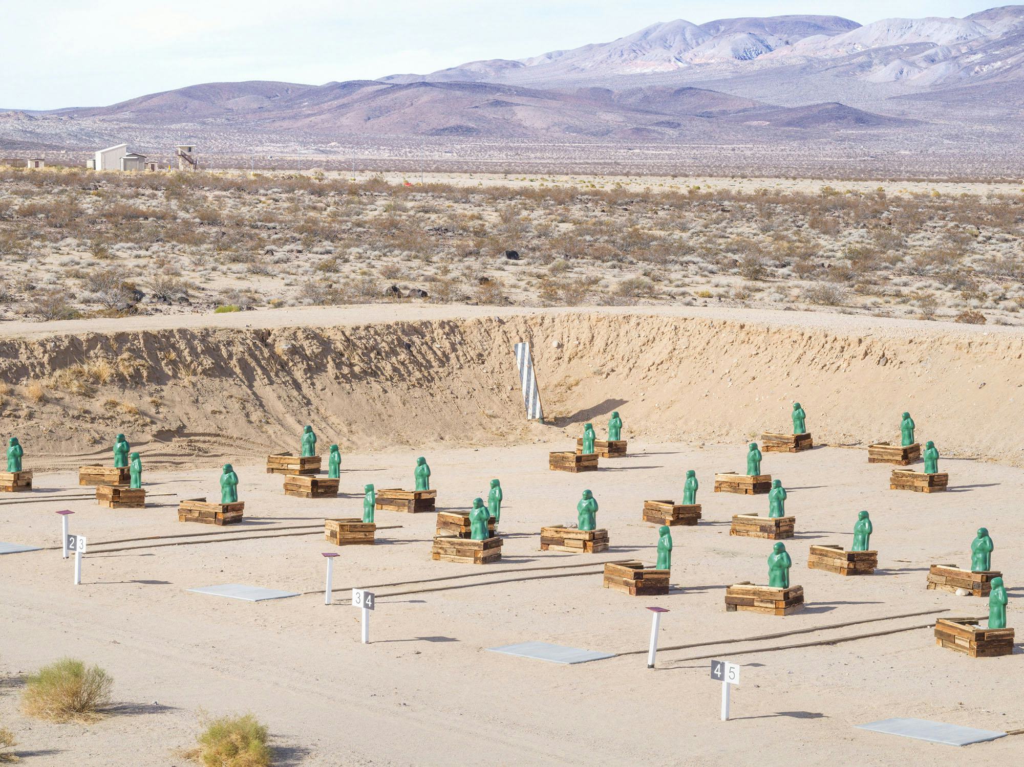 Shooting range with green figures lined up as targets, in the middle of a mountainous desert © Andrea Orejarena & Caleb Stein